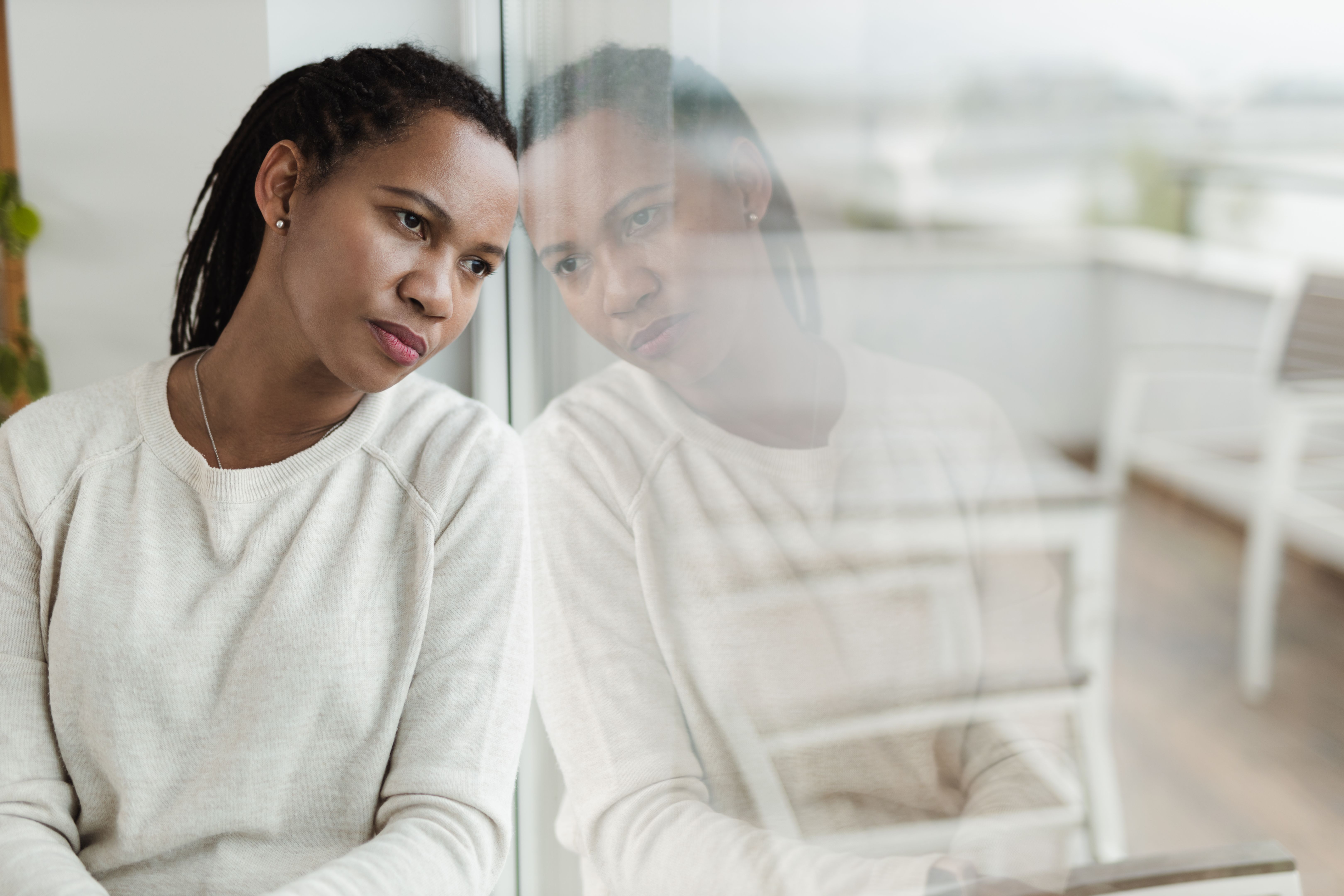 Pensive black woman looking through window from home. Pensive black woman looking through window from home.