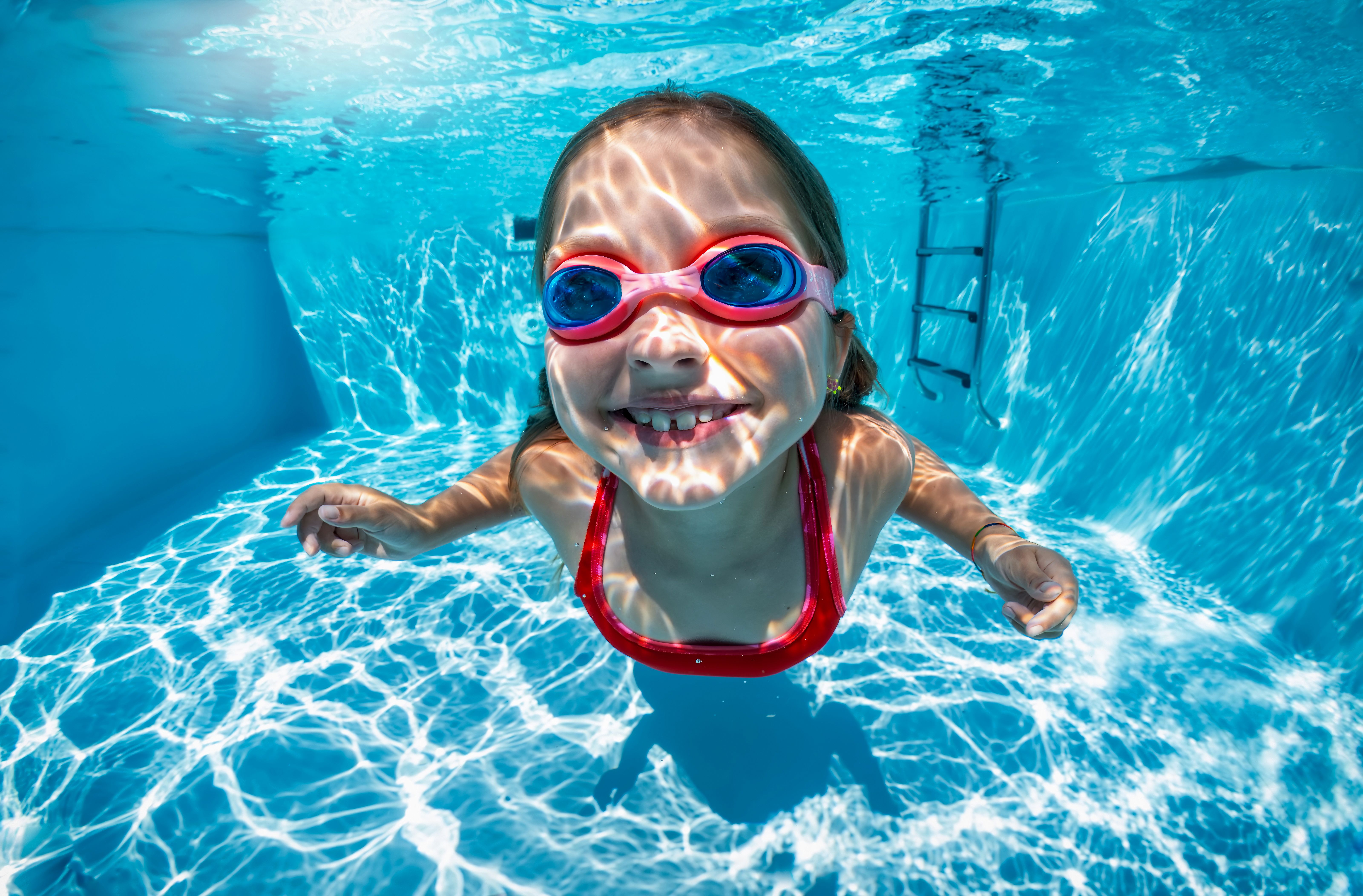 Funny portrait of a happy girl with goggles swimming under water