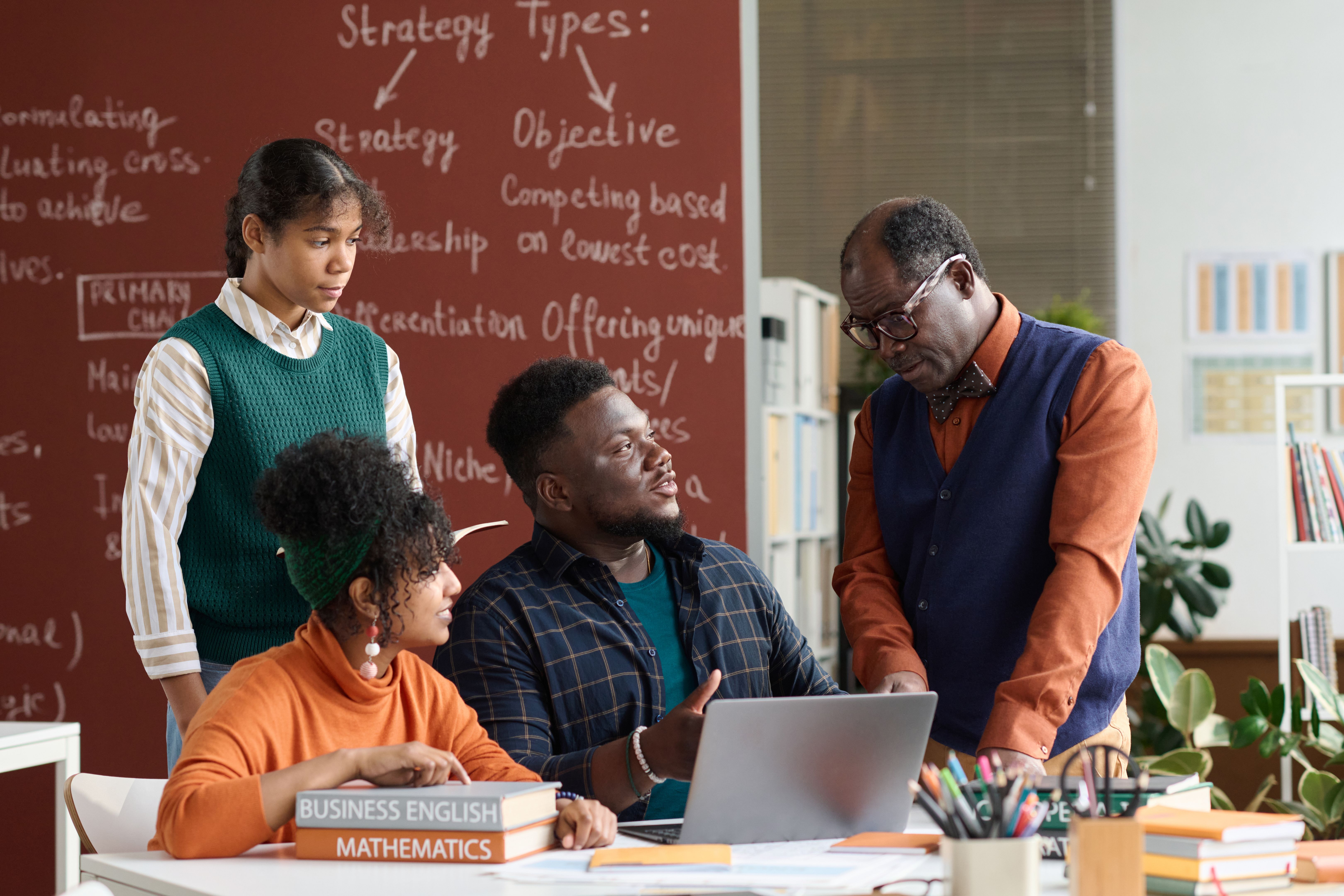 Senior Black Teacher Talking to Group of Students with Books and Computer Senior Black Teacher Talking to Group of Students with Books and Computer