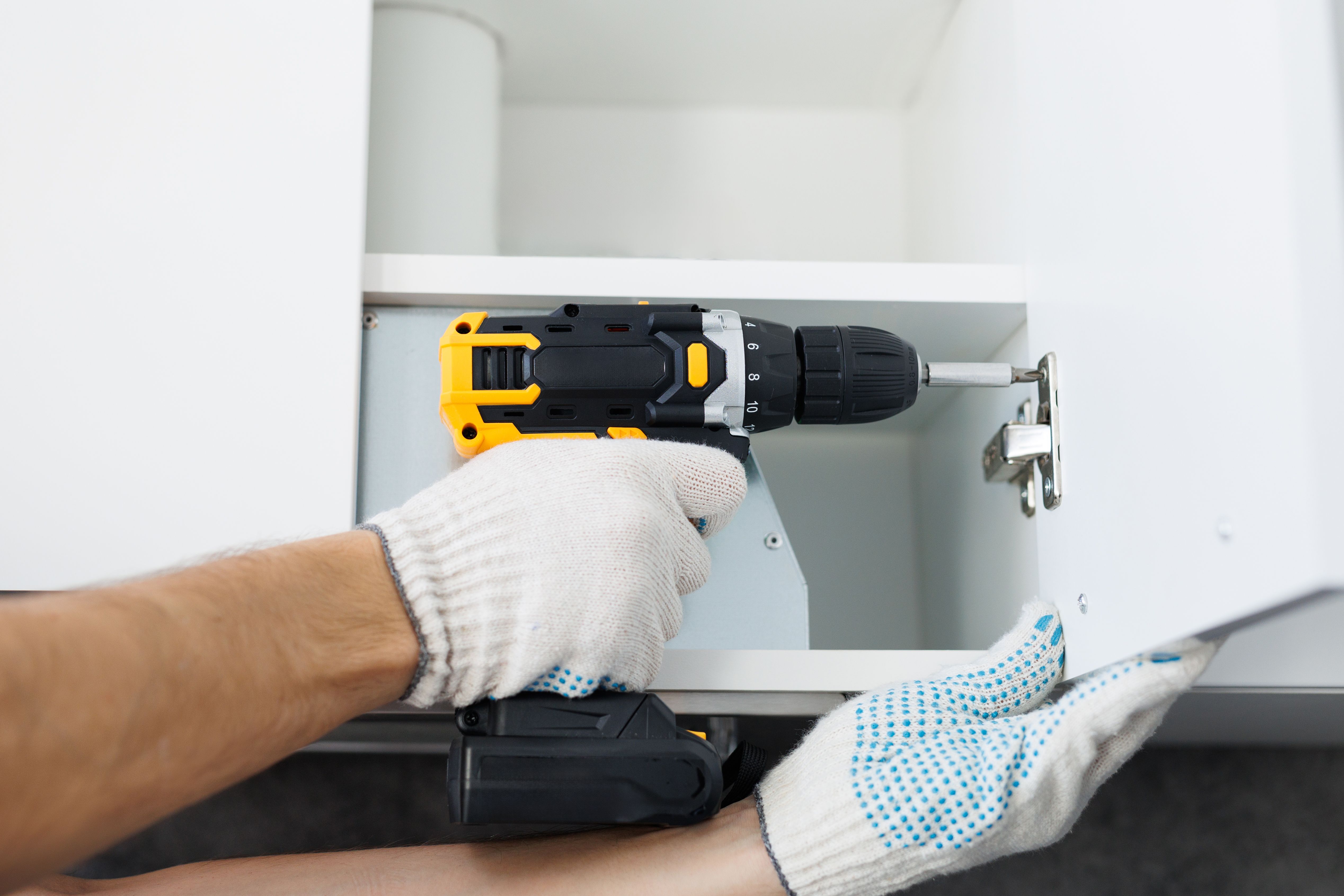 o insurubeaza balama usa cu manusi albe in timp ce monteaza o bucatarie. Prim-plan de masina de insurubat cu manusi albe.