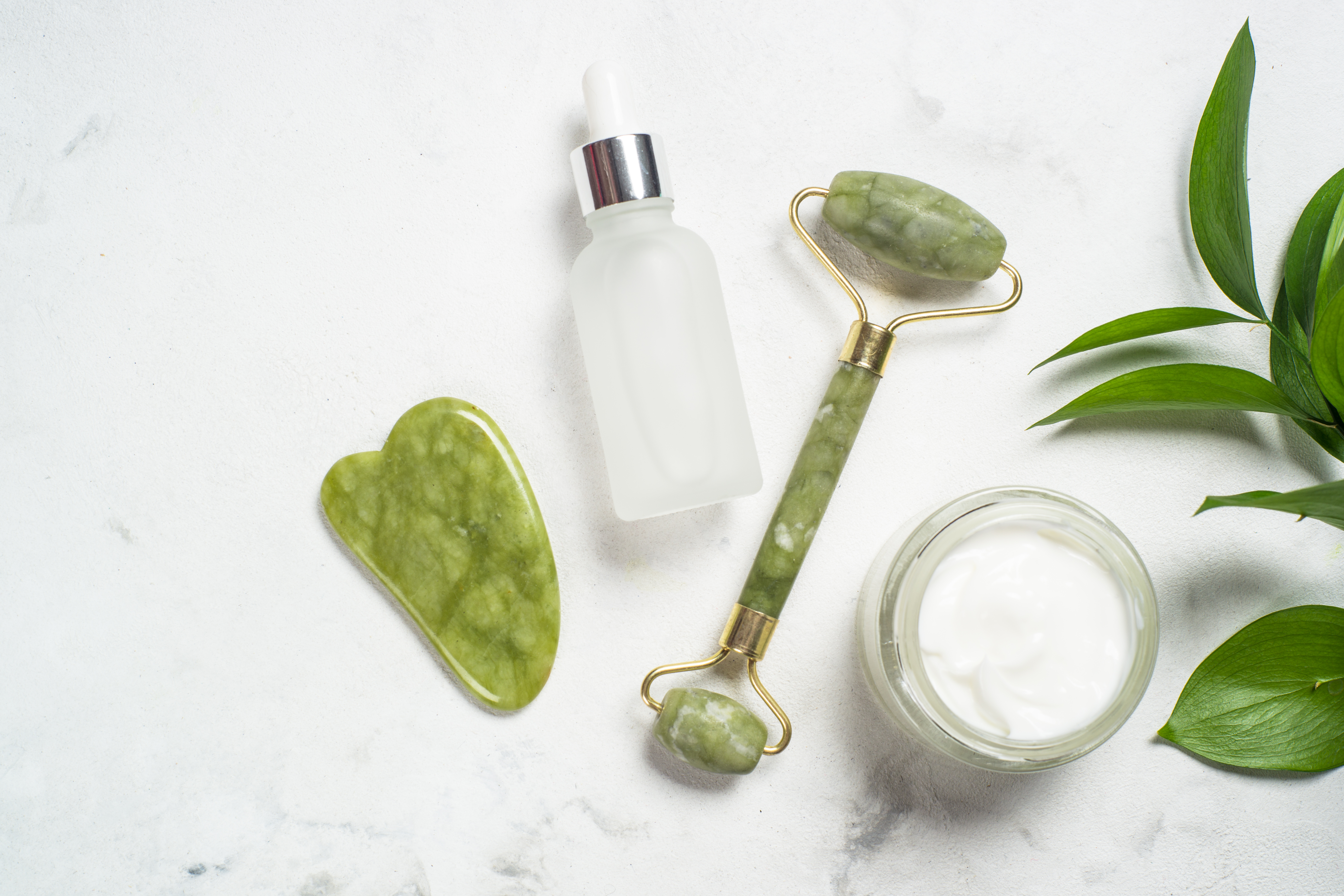 Jade roller and gua sha stone massager with face cream and serum bottle.