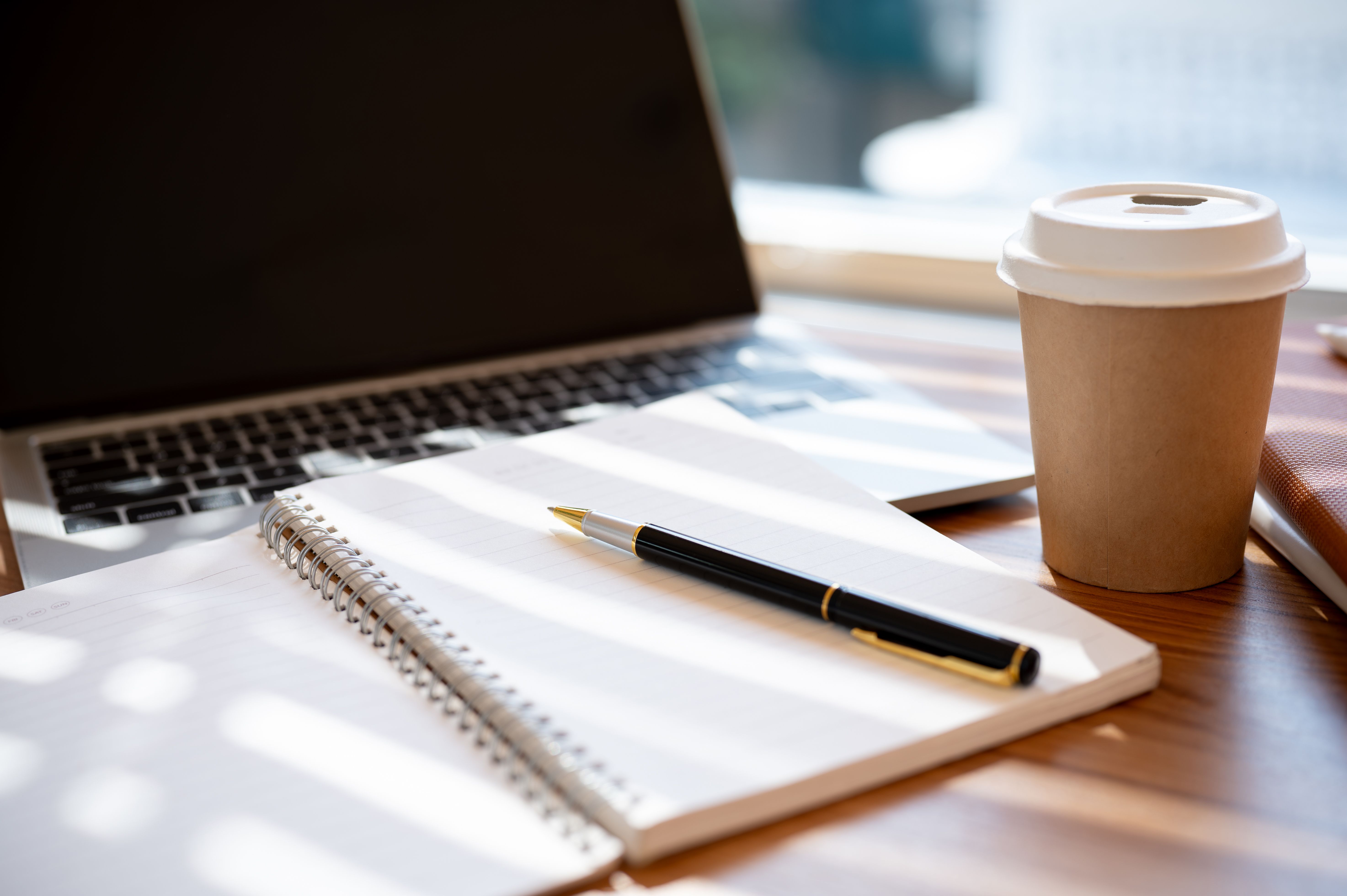 A wooden table with an opened book, a pen, a laptop, and a coffee cup. workspace in a cafe concept