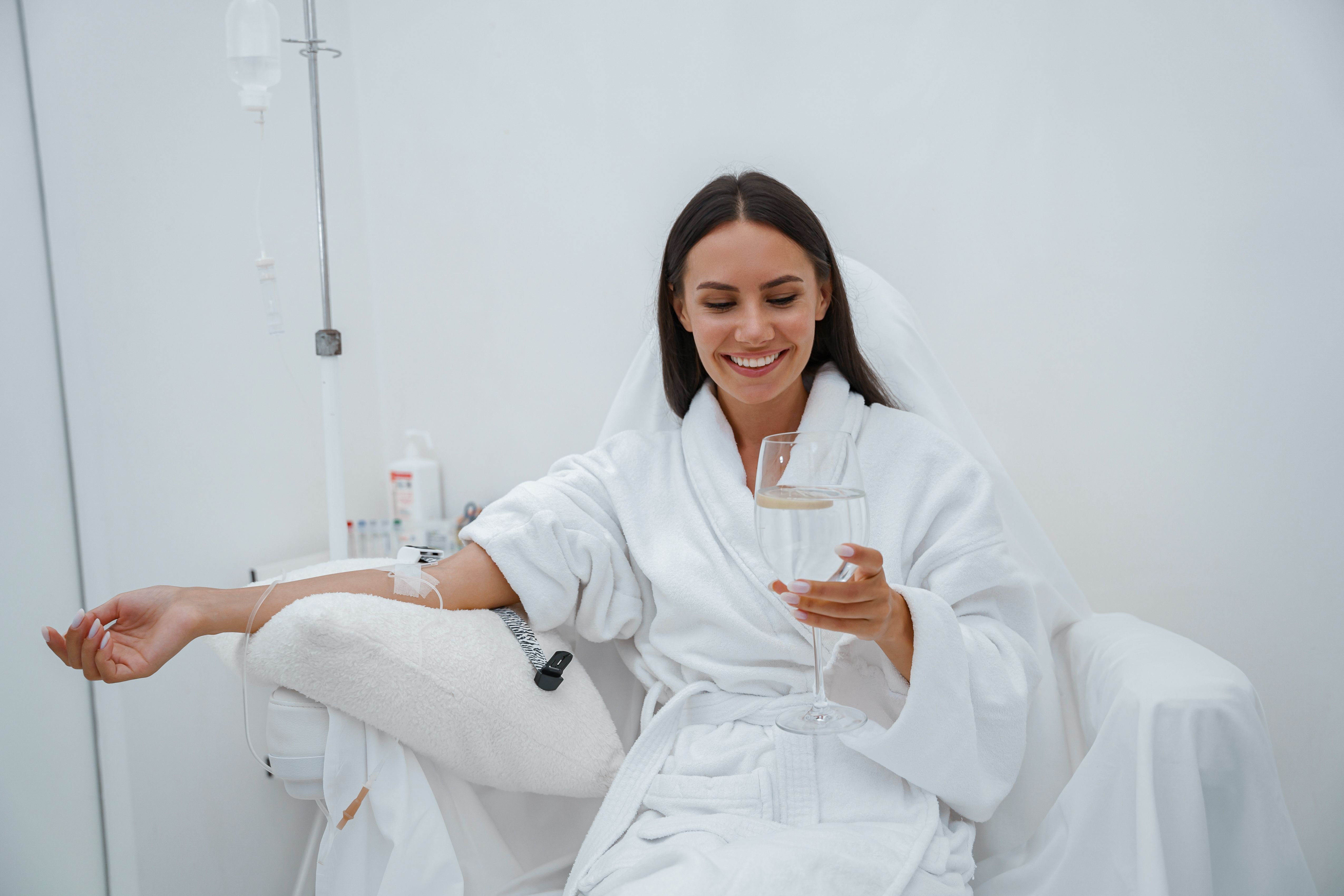 Beautiful woman in white bathrobe drink water during medical procedure in beauty clinic Beautiful woman in white bathrobe drink water during medical procedure in beauty clinic