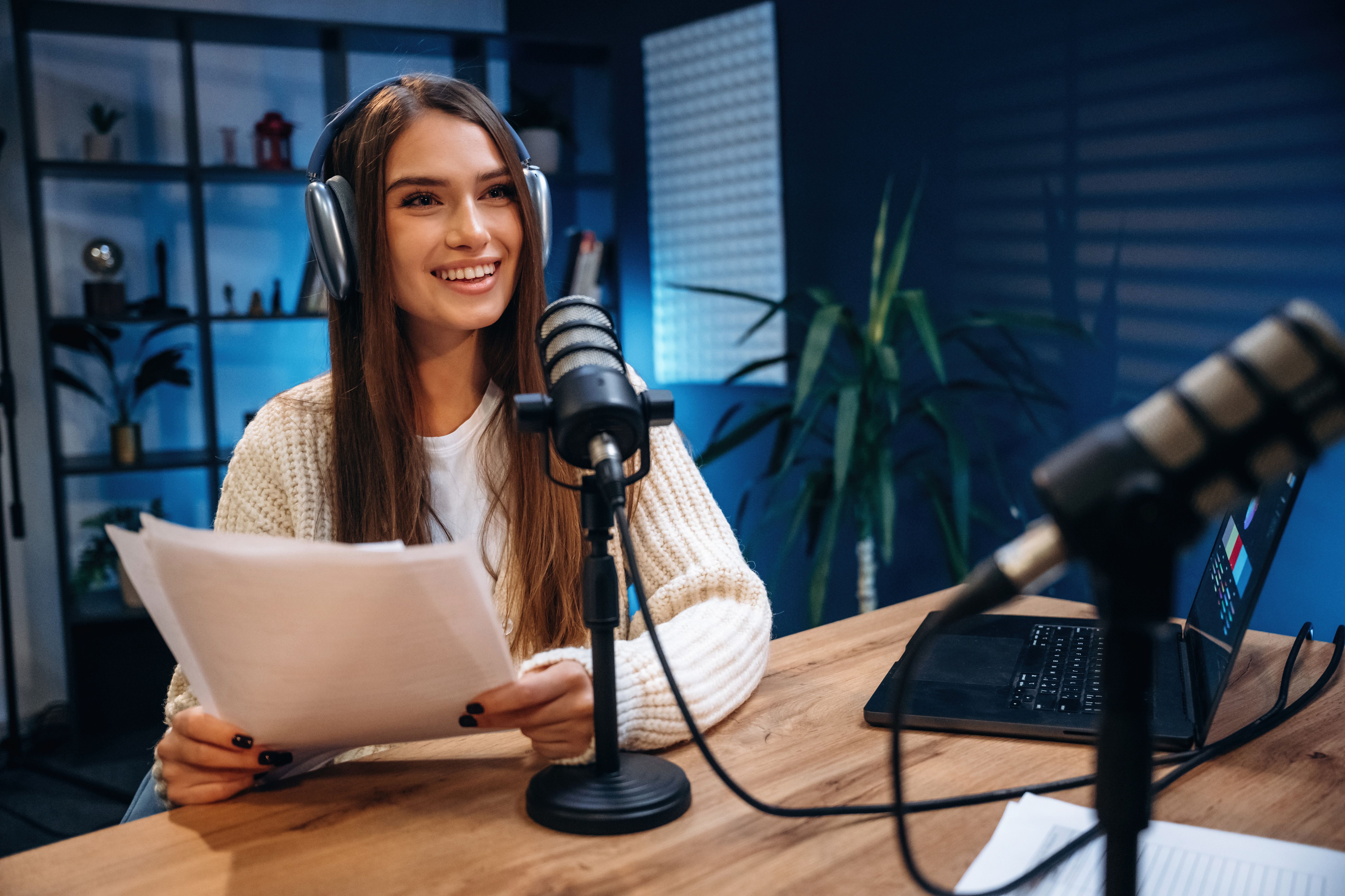 Vista frontal, sentado. La mujer presenta un podcast de radio con micrófono y computadora portátil
