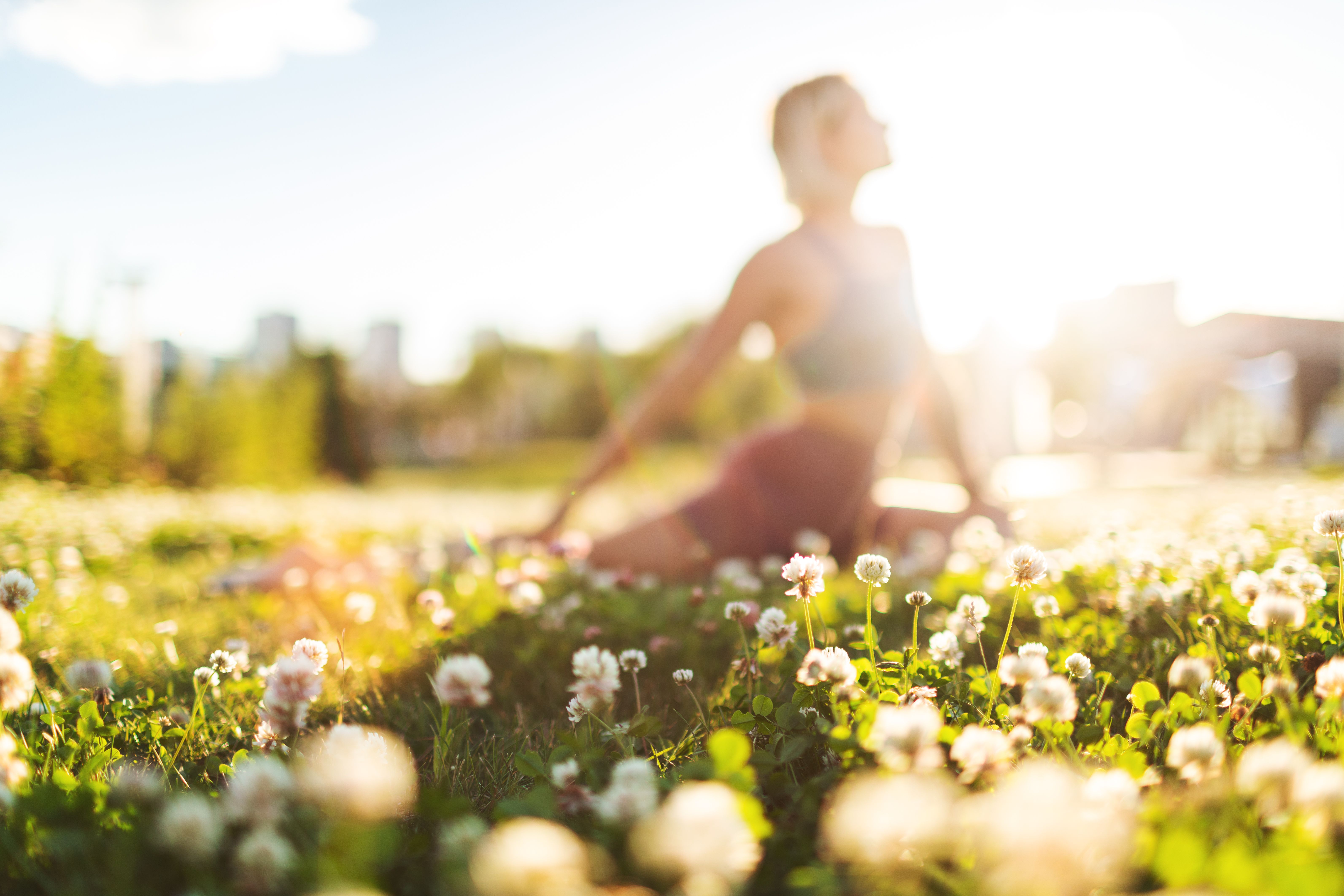 Young adult woman practicing yoga outdoors in park at sunset