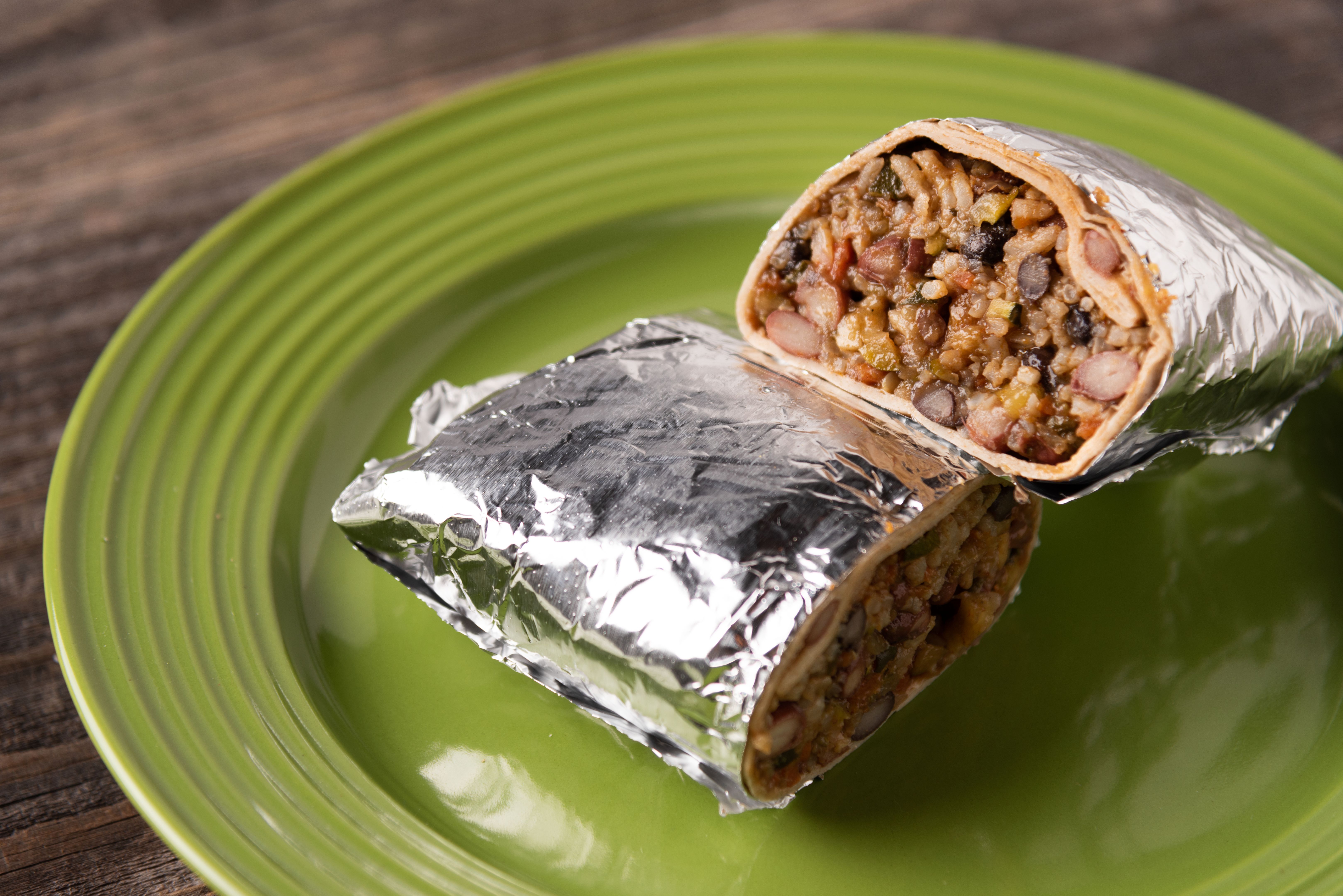 Burrito wrapped in foil cut in half served on a green plate on a reclaimed wood table. Burrito wrapped in foil cut in half served on a green plate on a reclaimed wood table.
