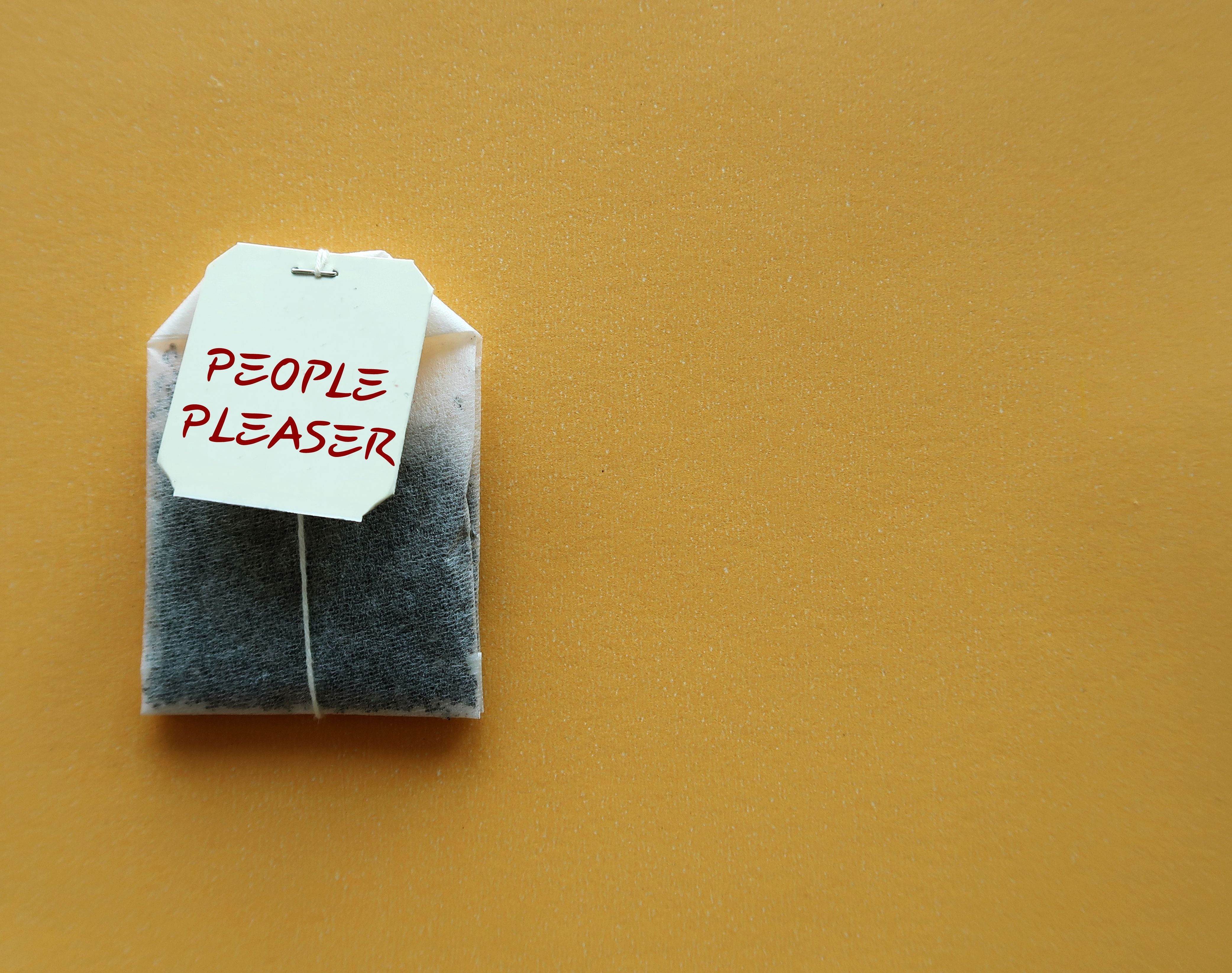 Teabag on yellow copy space background with text PEOPLE PLEASER, concept of one who tries hard to make others happy even go out of their way, time or resources,overly concerned with pleasing others