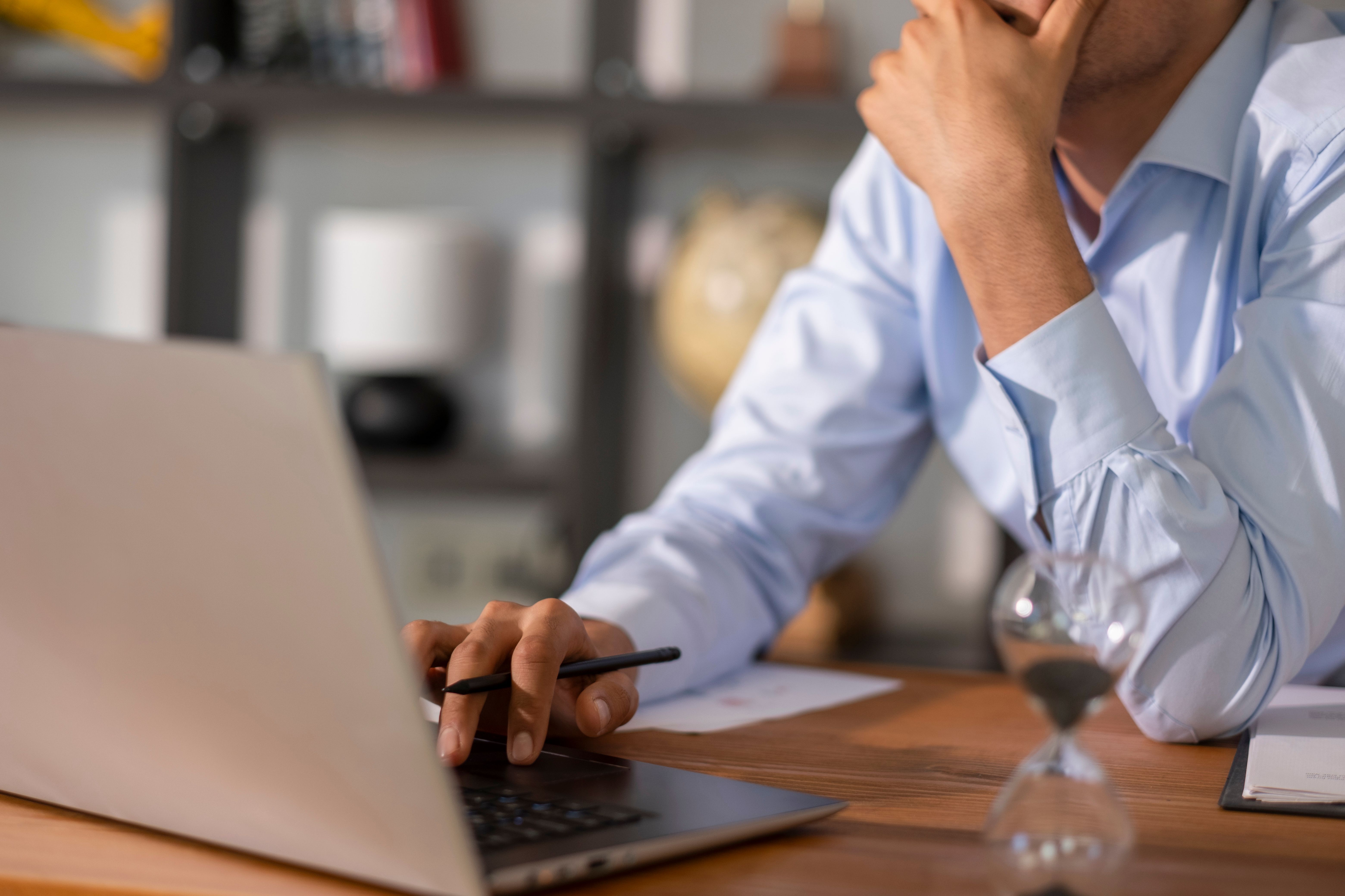 Due diligence by businessman using laptop at office desk with hourglass, working under pressure