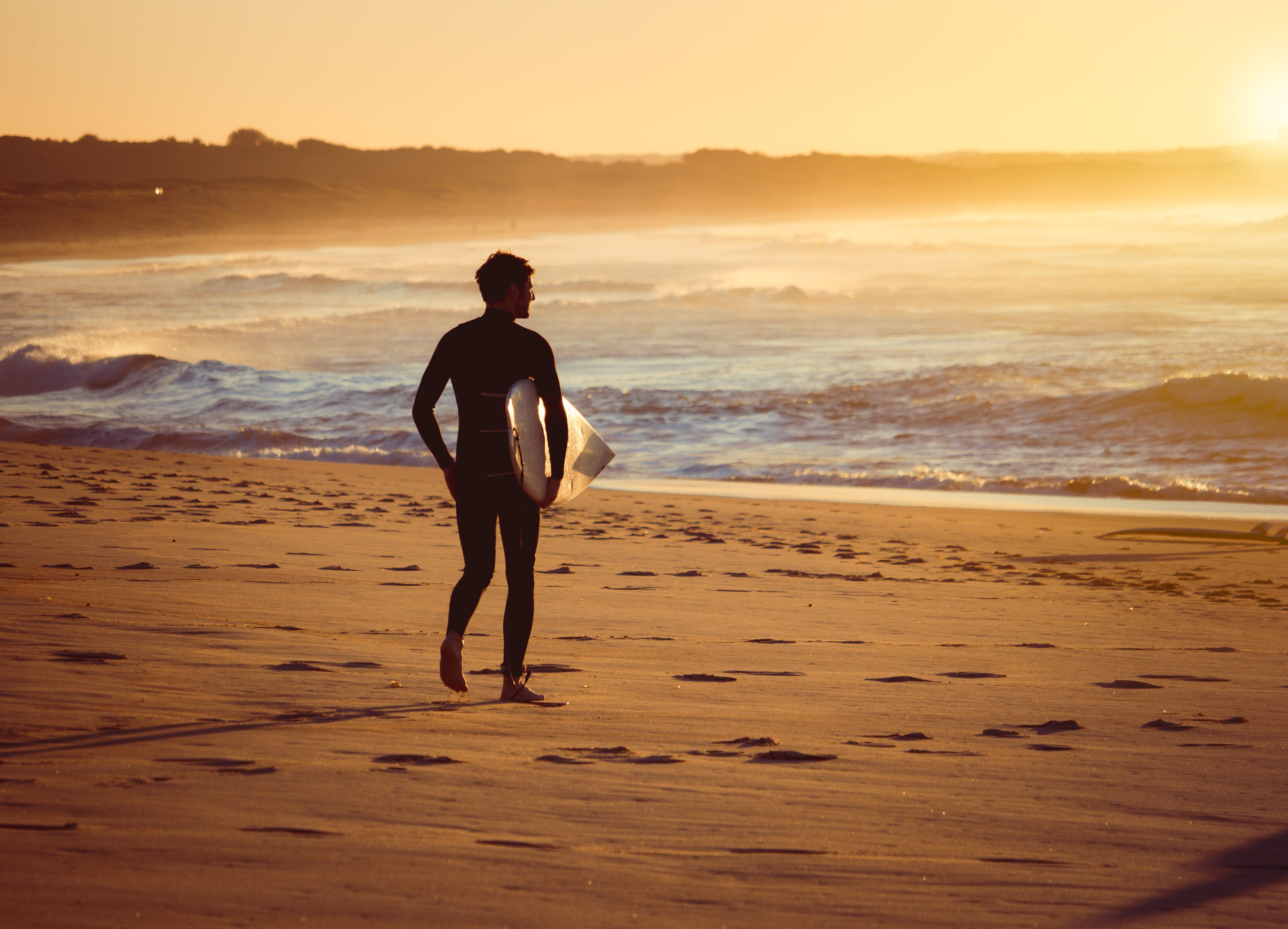 Surfer walking observing the surf on a beach at sunrise