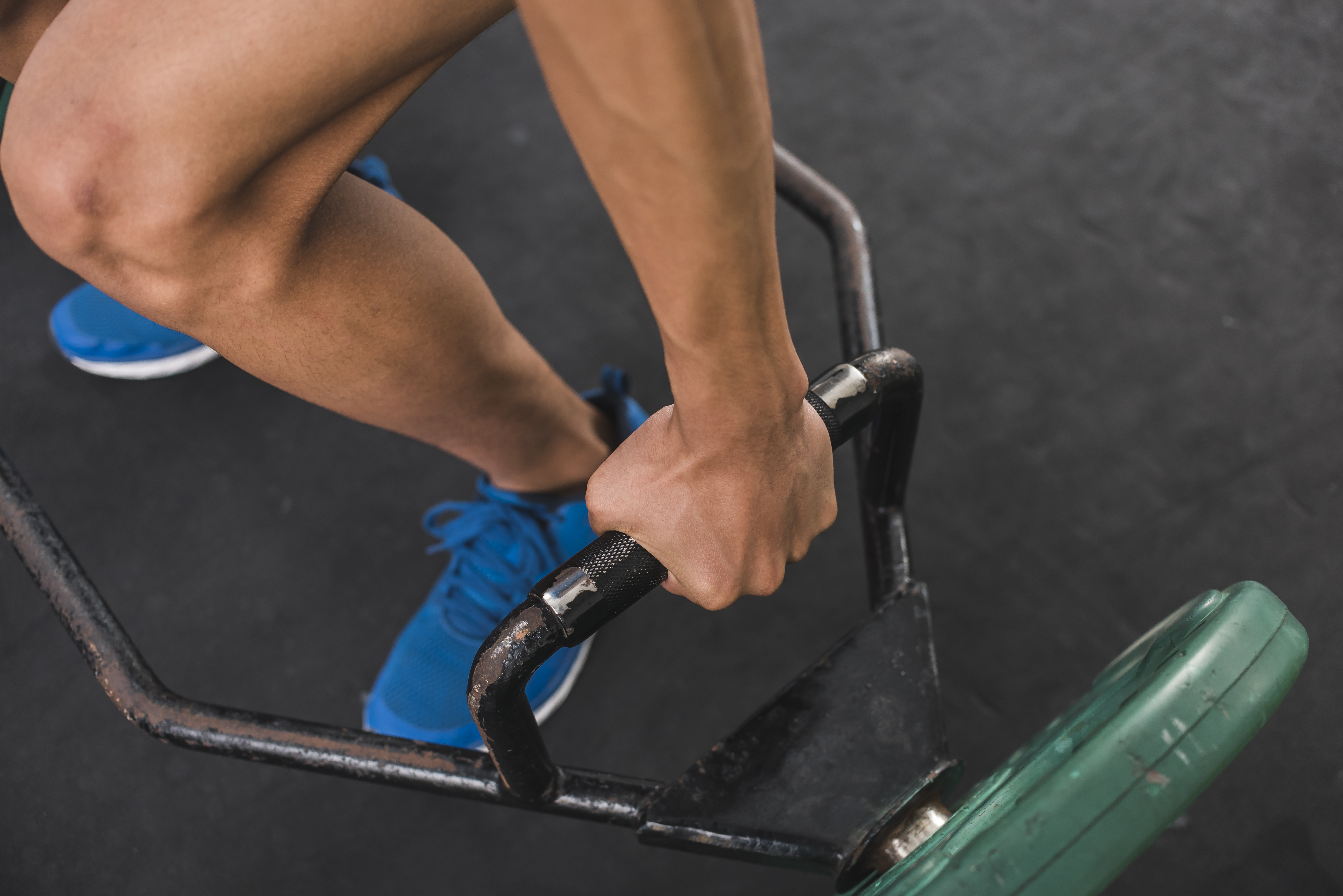 An anonymous young man gripping a hex bar on the floor. Preparing to do deadlifts at the gym. Upper body workout.