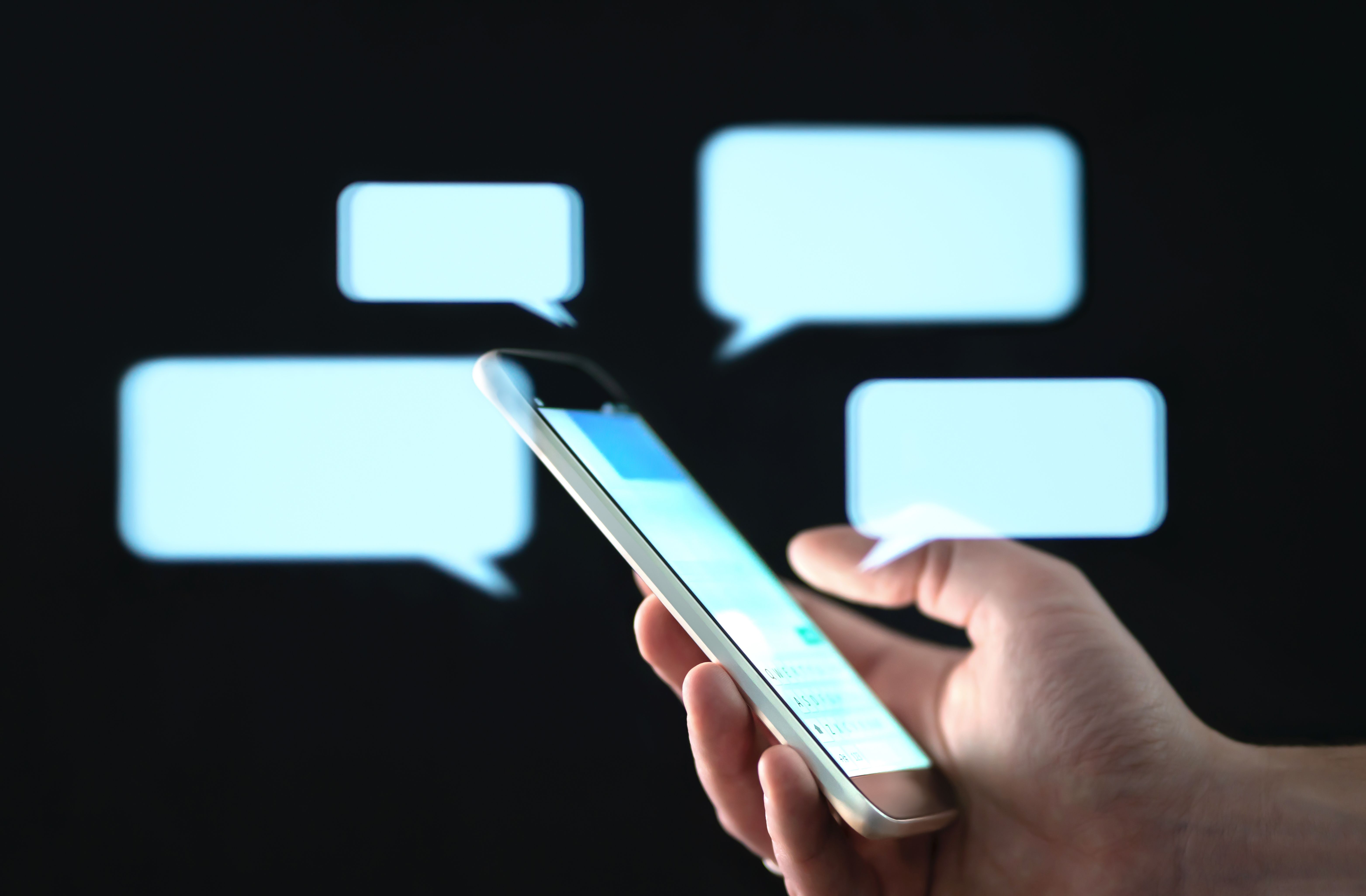 Text messages in cellphone screen with abstract hologram speech bubbles. Instant messaging app. Texting, group chat, sexting or sms concept. Text messages in cellphone screen with abstract hologram speech bubbles. Instant messaging app. Texting, group chat, sexting or sms concept.