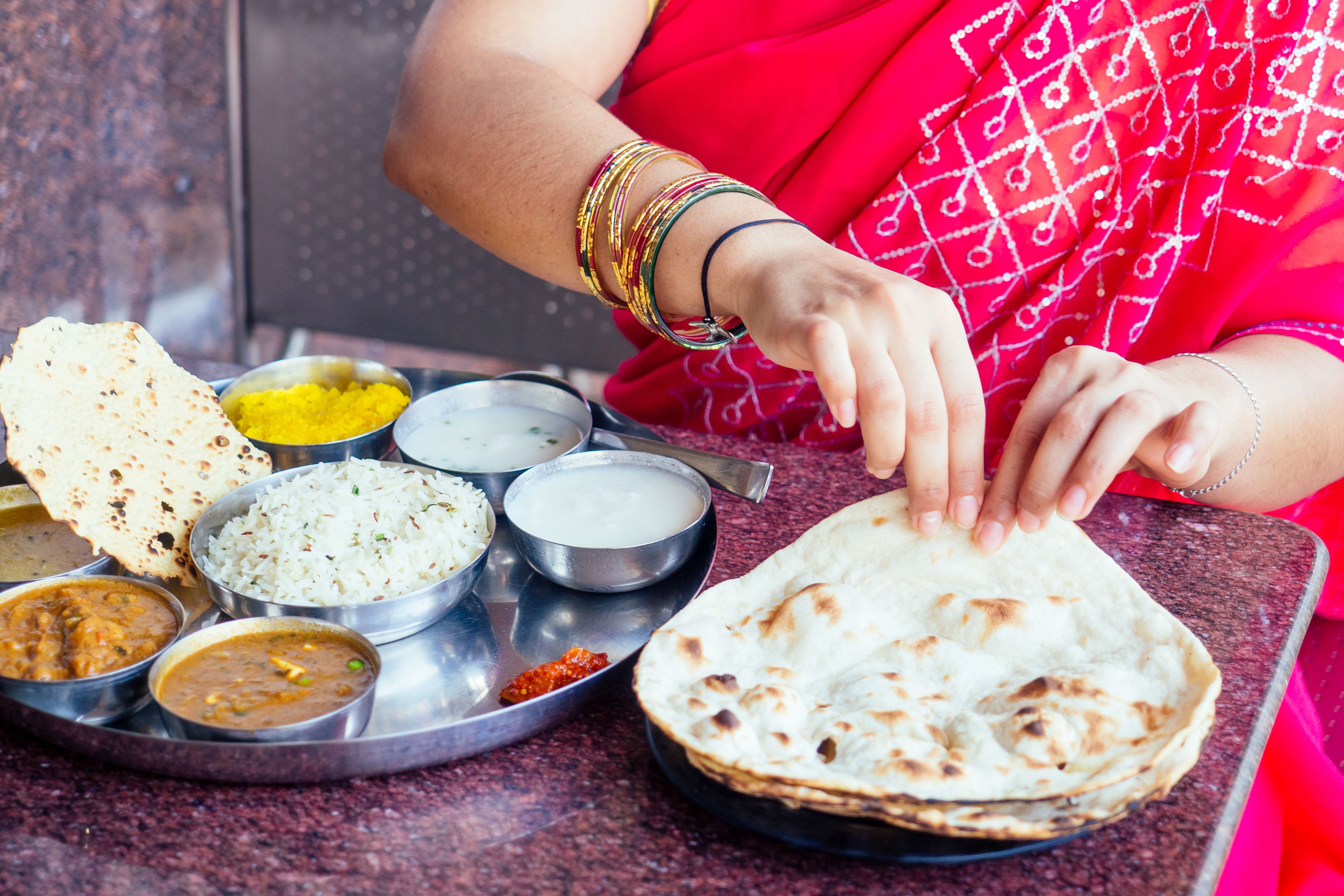 close up photo of Indian traditional vegetarian thali from rice, dal, potatoes, tomato salad on metal plate ,female hands roti india tortilla Chapati