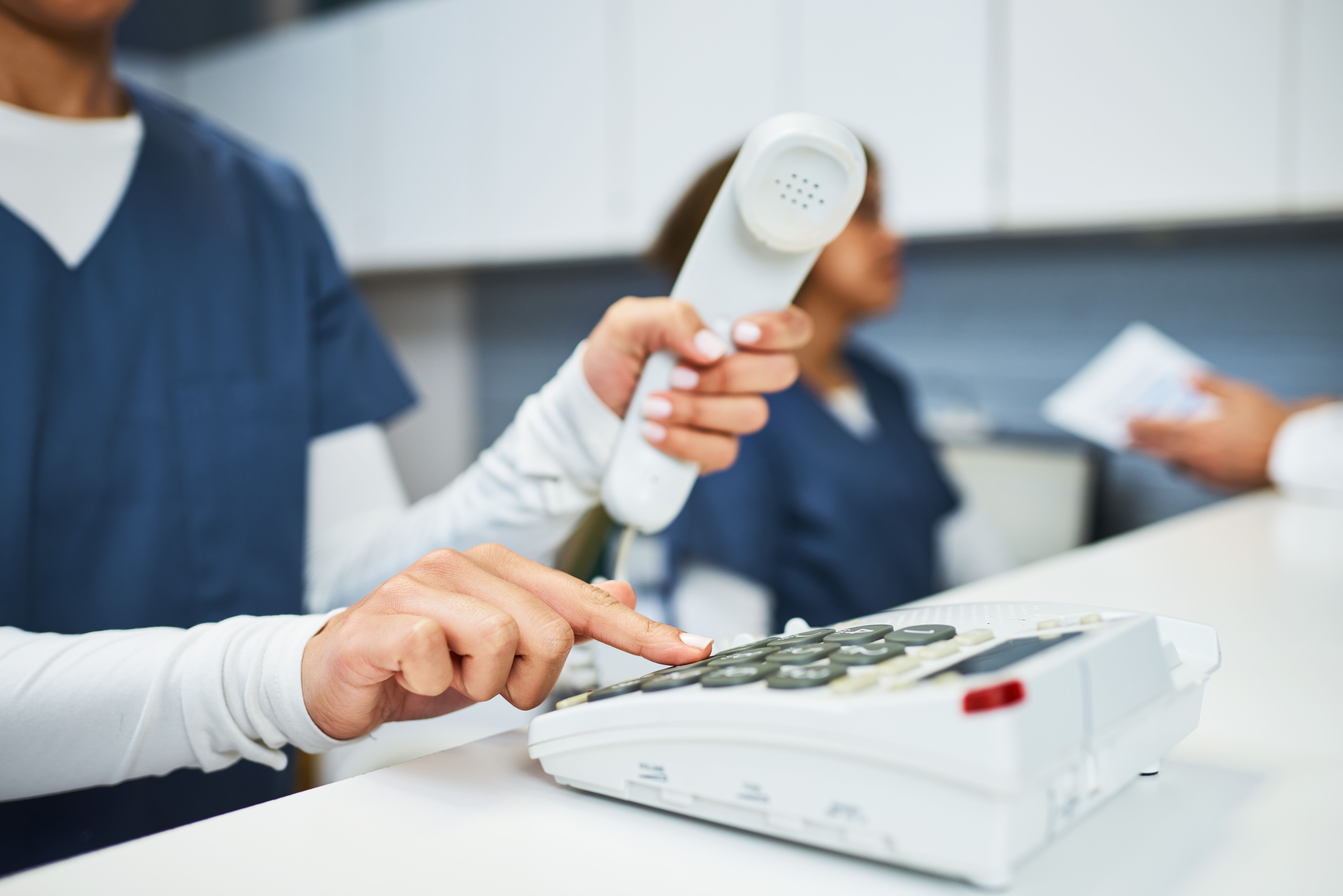 Healthcare Receptionist Dialing a Phone Number in a Medical Office Setting