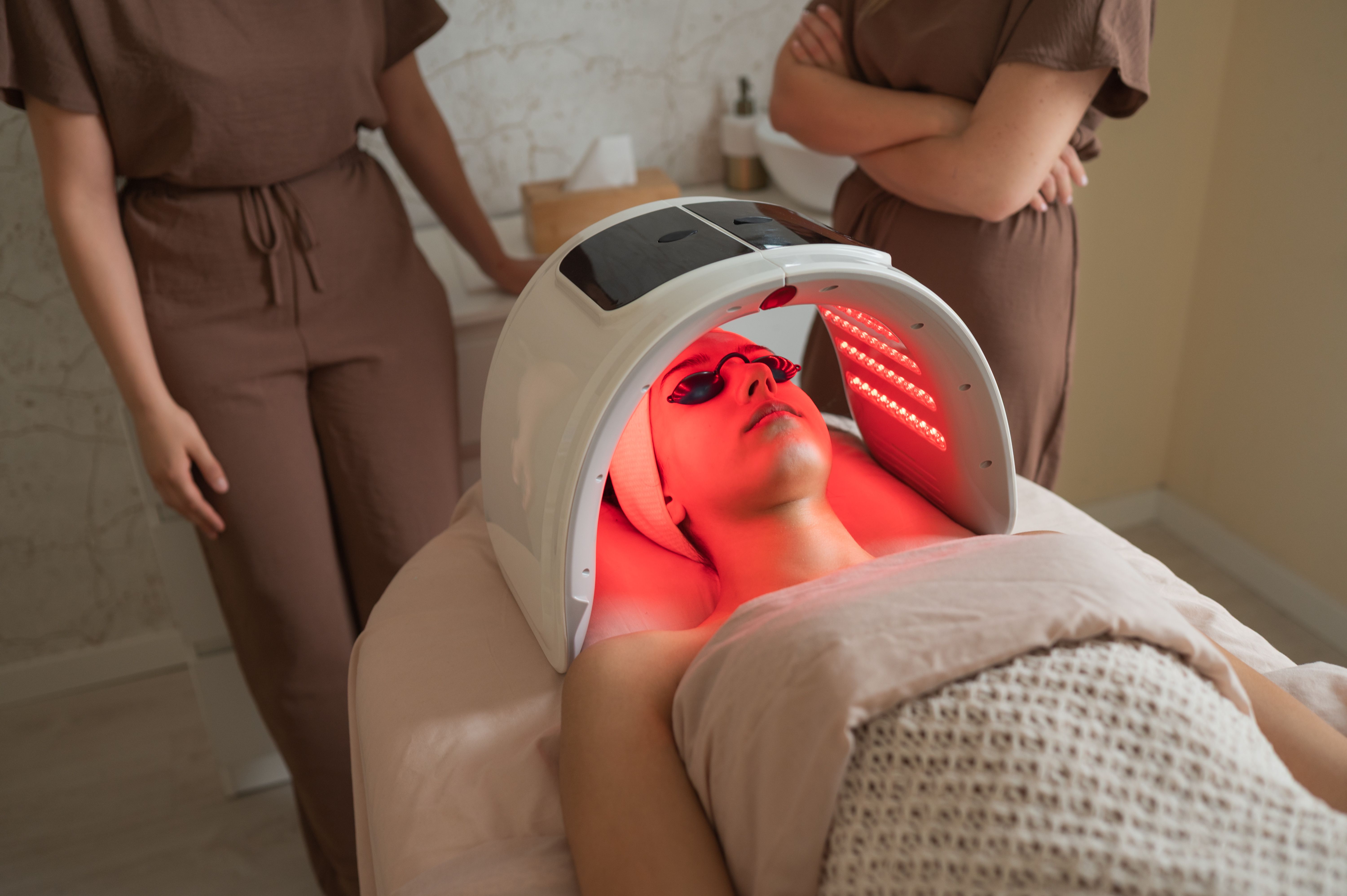 Beauticians observing client receiving led light therapy facial treatment Beauticians observing client receiving led light therapy facial treatment