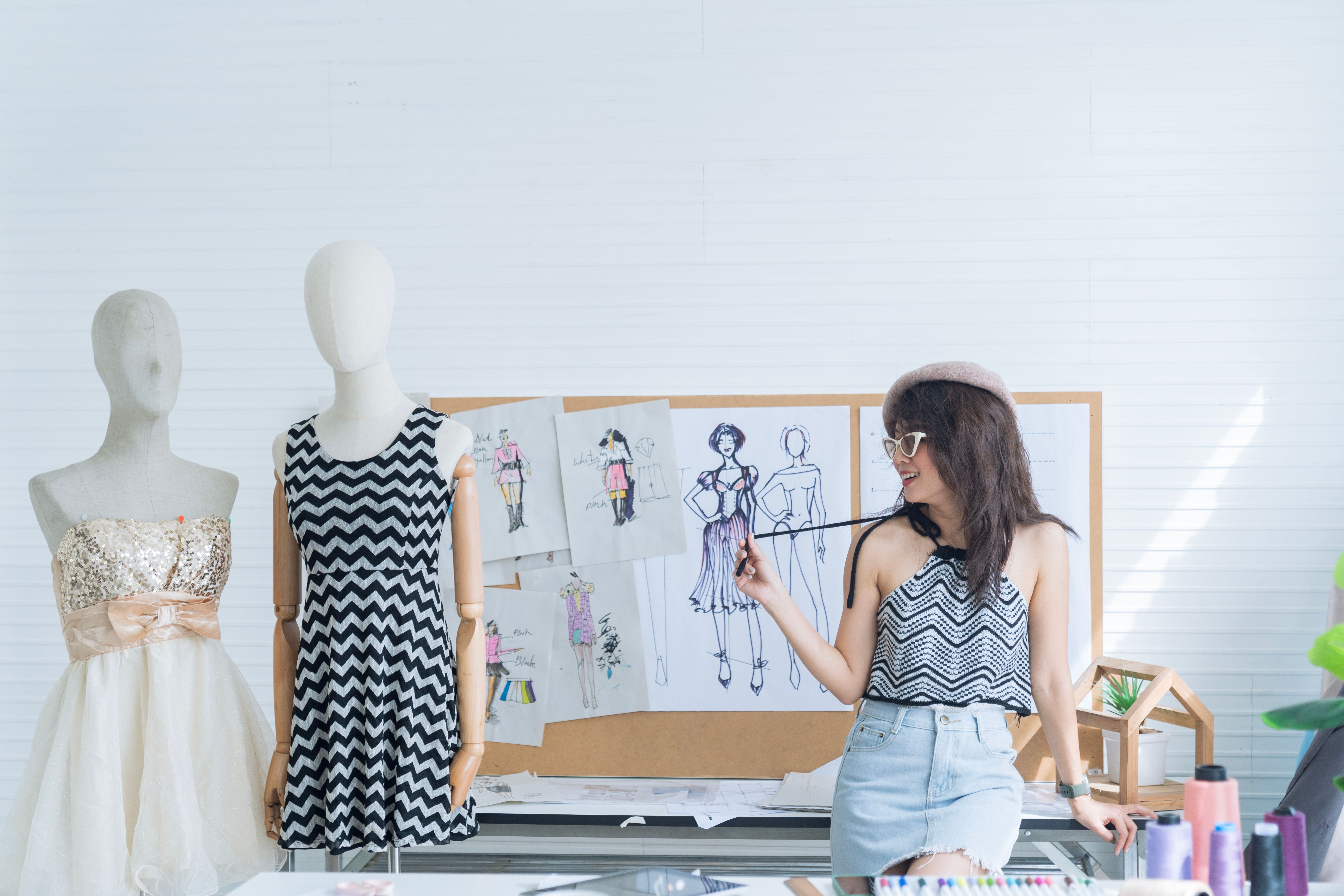 Fashion designers working in studio sitting on the desk. Asian female fashion designer on creation inspiration.