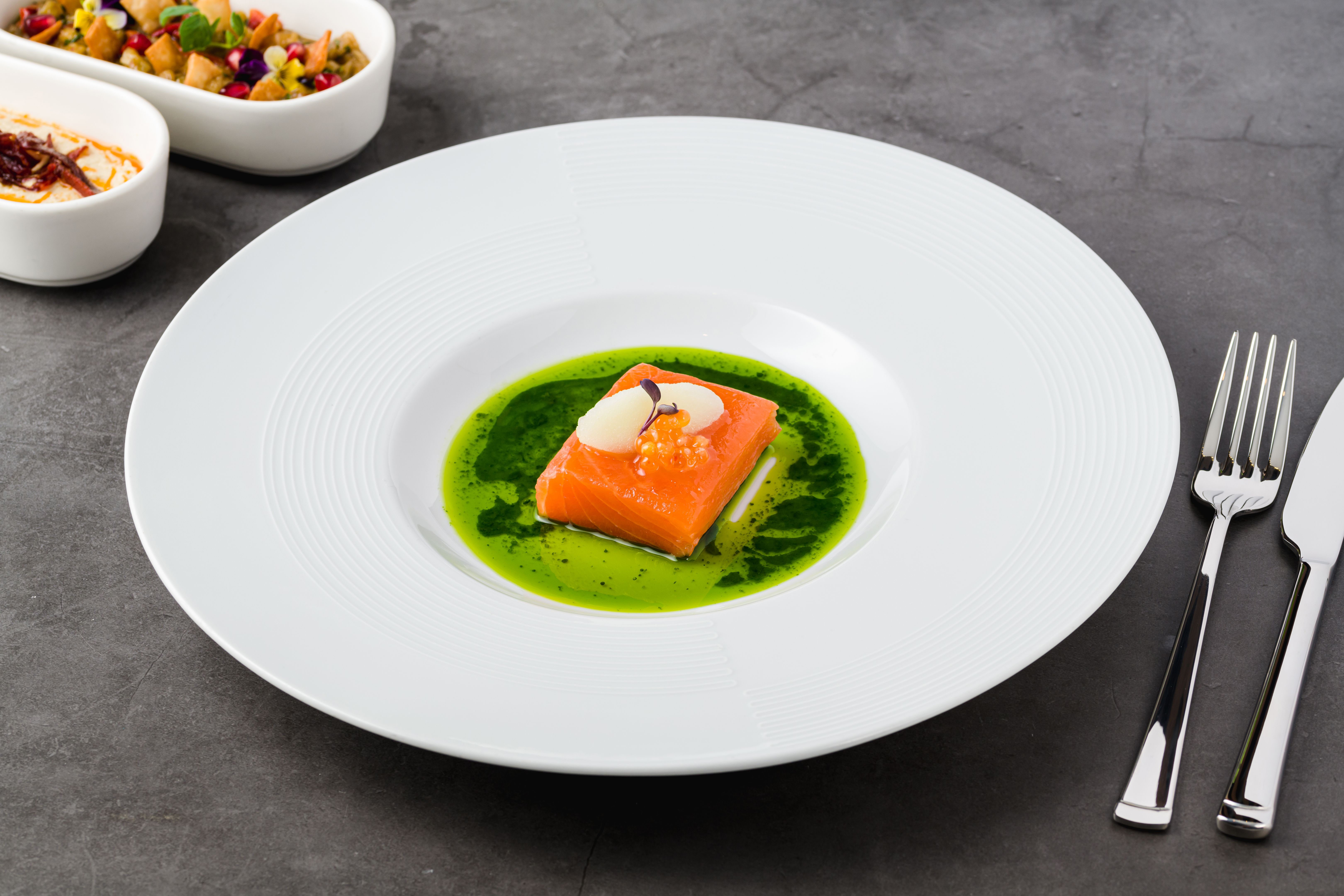 Sous-vide salmon fillet with fish roe, garnished with sorbet and microgreens, served on a vibrant green herb sauce