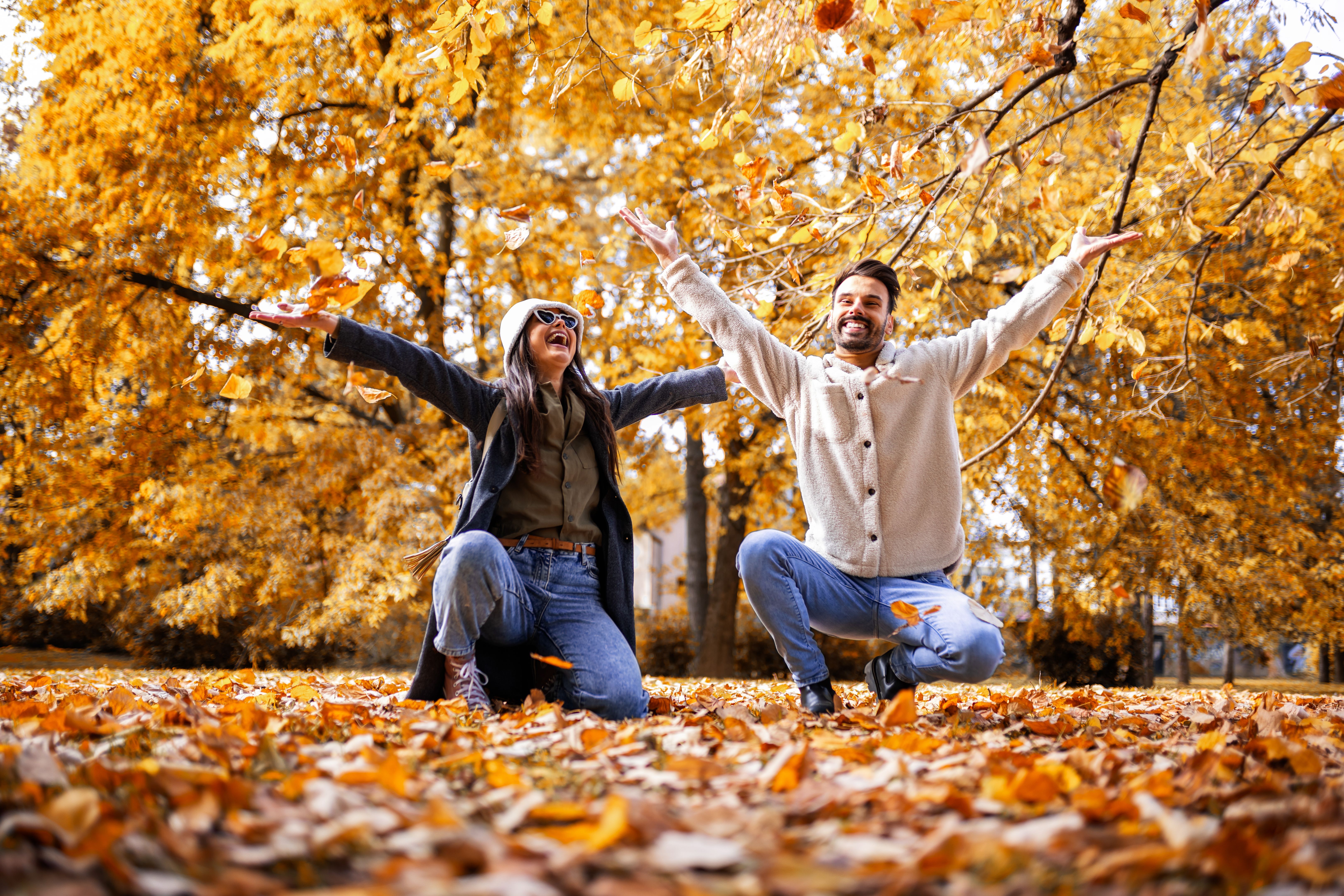 Happy young couple playfully throwing colorful autumn leaves in park, enjoying romantic fall day together. Happy young couple playfully throwing colorful autumn leaves in park, enjoying romantic fall day together.