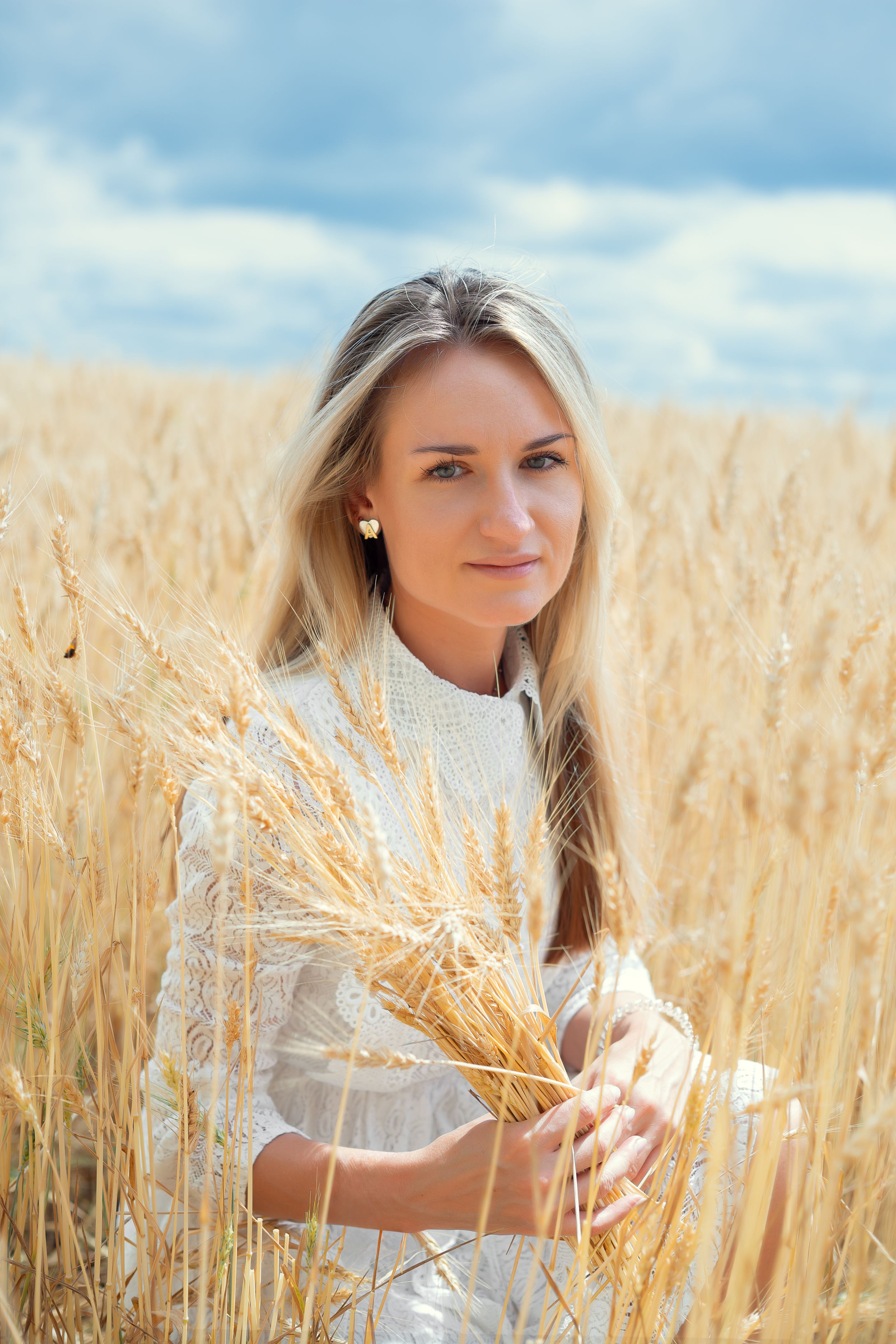 Young blonde woman holding wheat in a field under a cloudy sky