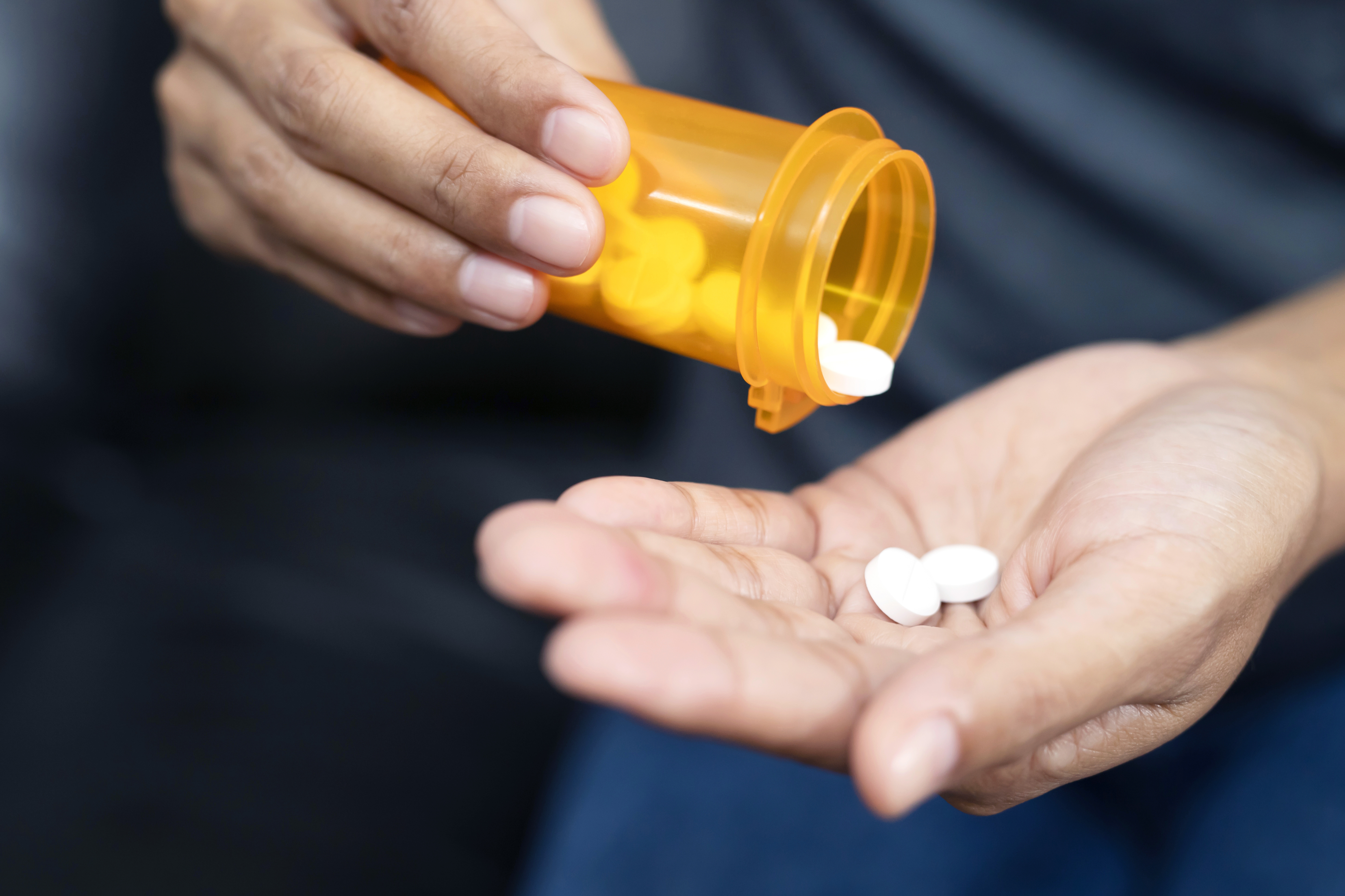 Woman hand with pills on, spilling pills out of bottle on dark background. Woman hand with pills on, spilling pills out of bottle on dark background.