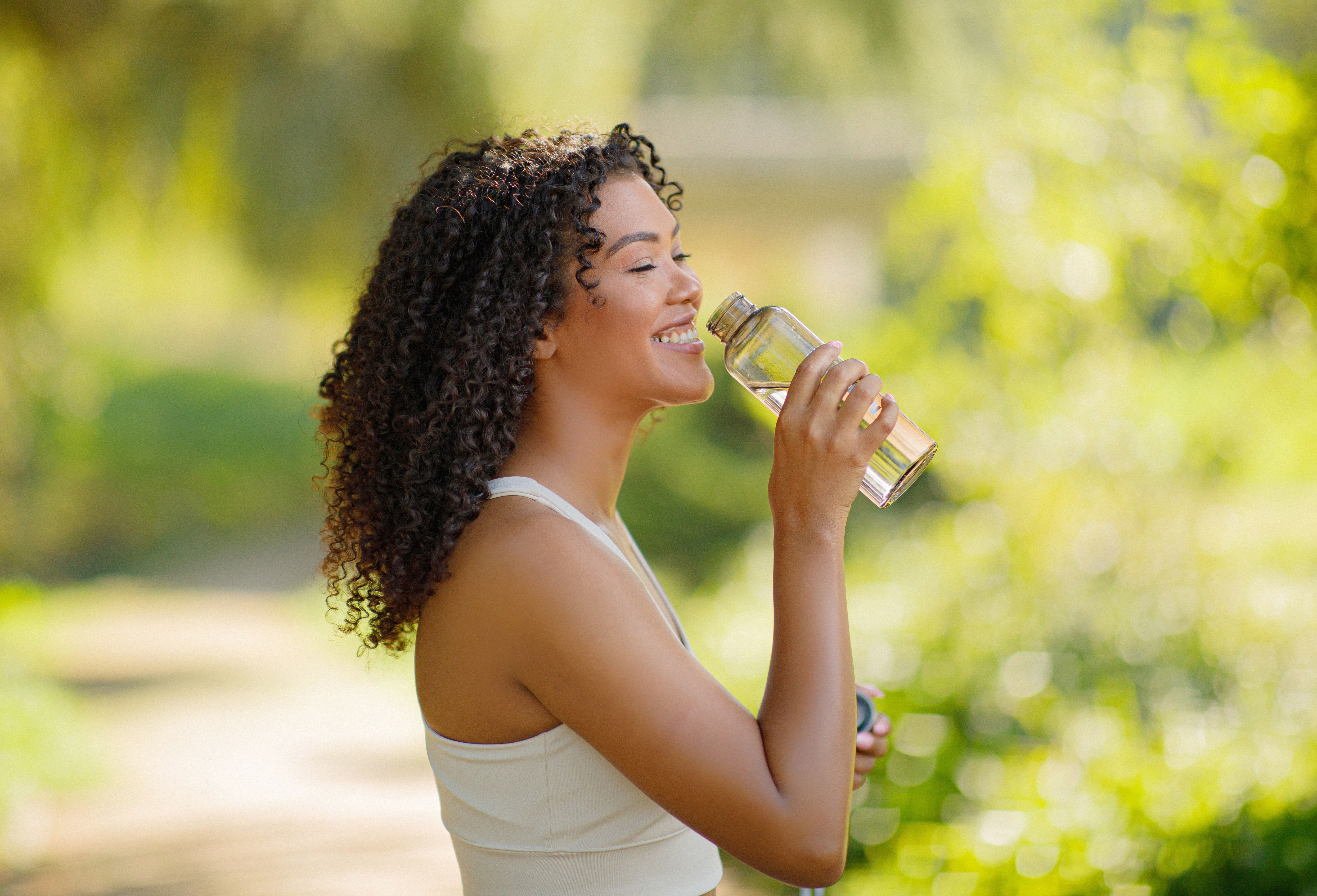 Brasilianische Fitness-Dame genießt das Trinken von Wasser aus der Flasche im Freien