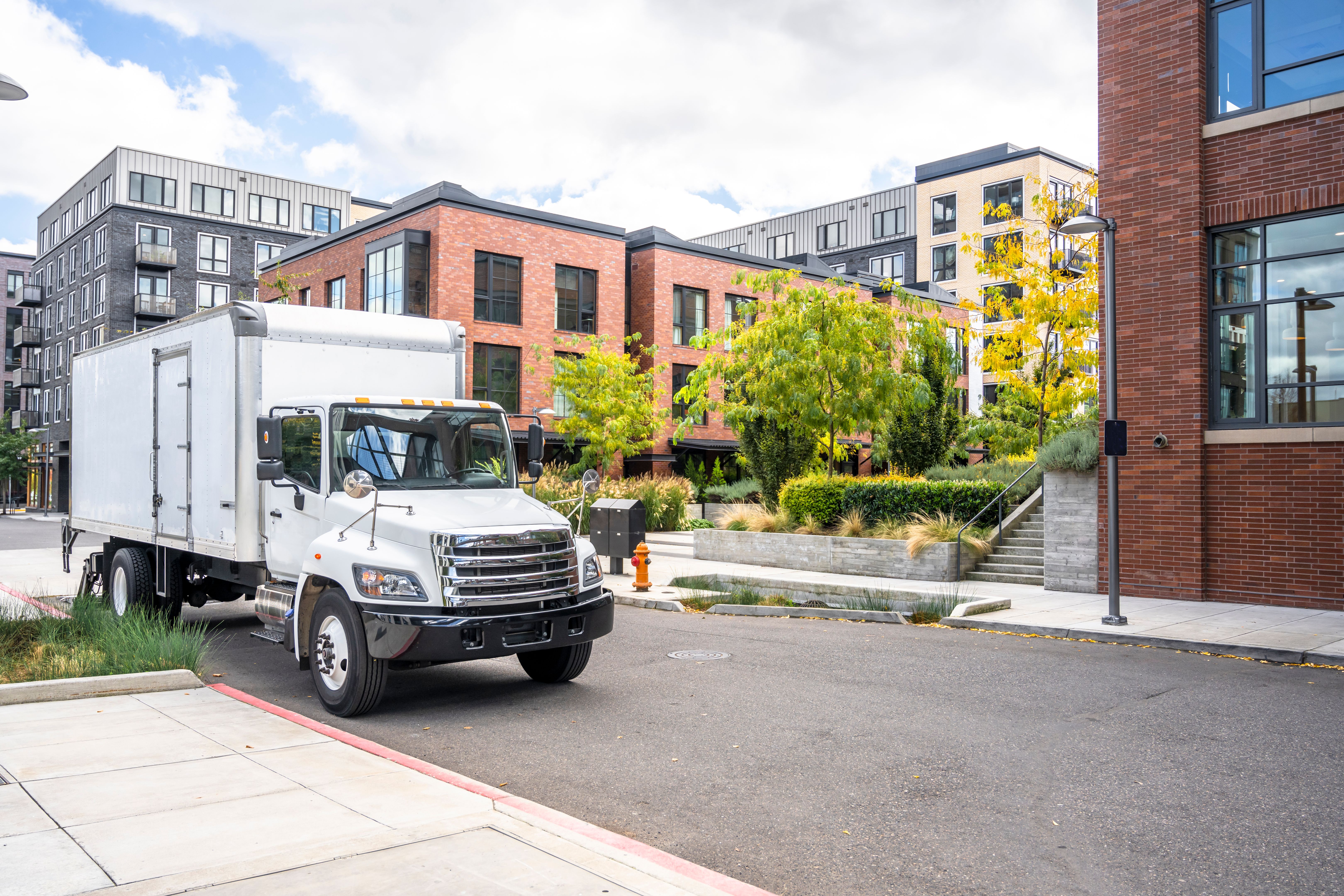 Middle size rig semi truck with box trailer standing on the city street with urban multilevel apartment buildings unloading delivered goods