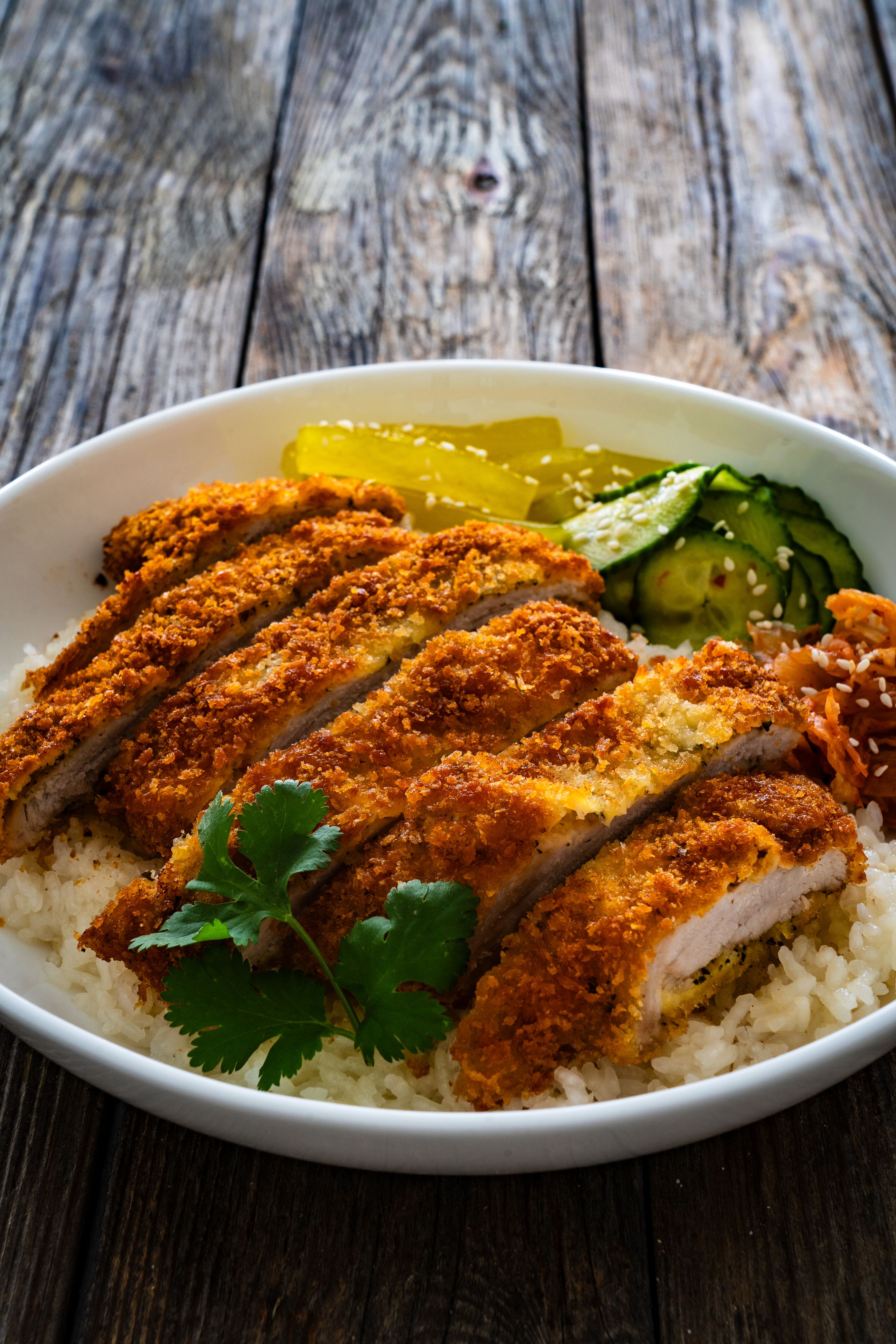 Torikatsu - crispy Japanese chicken cutlet with white rice and cucumber on wooden table