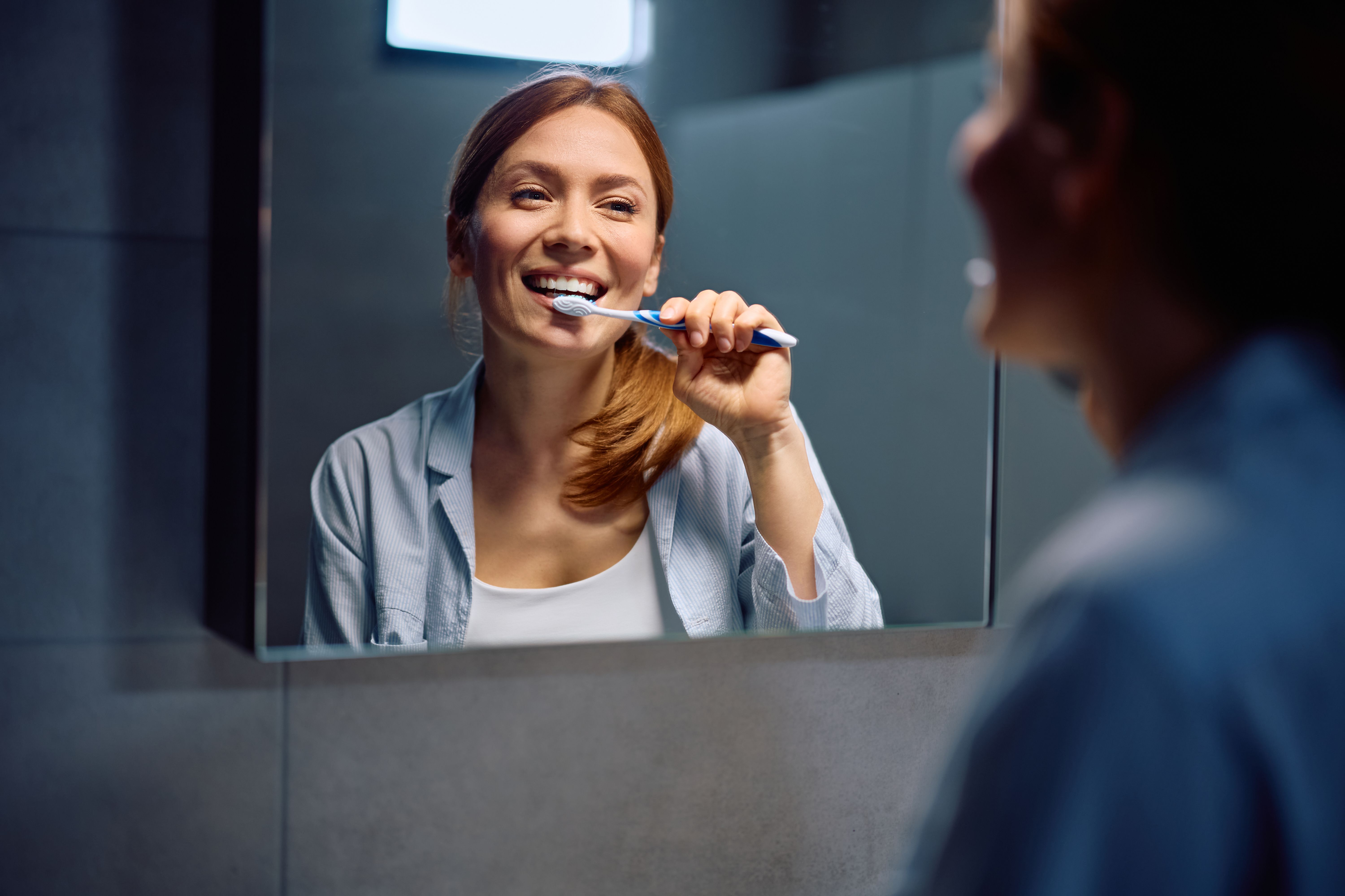 Happy woman brushing her teeth in front of a mirror.