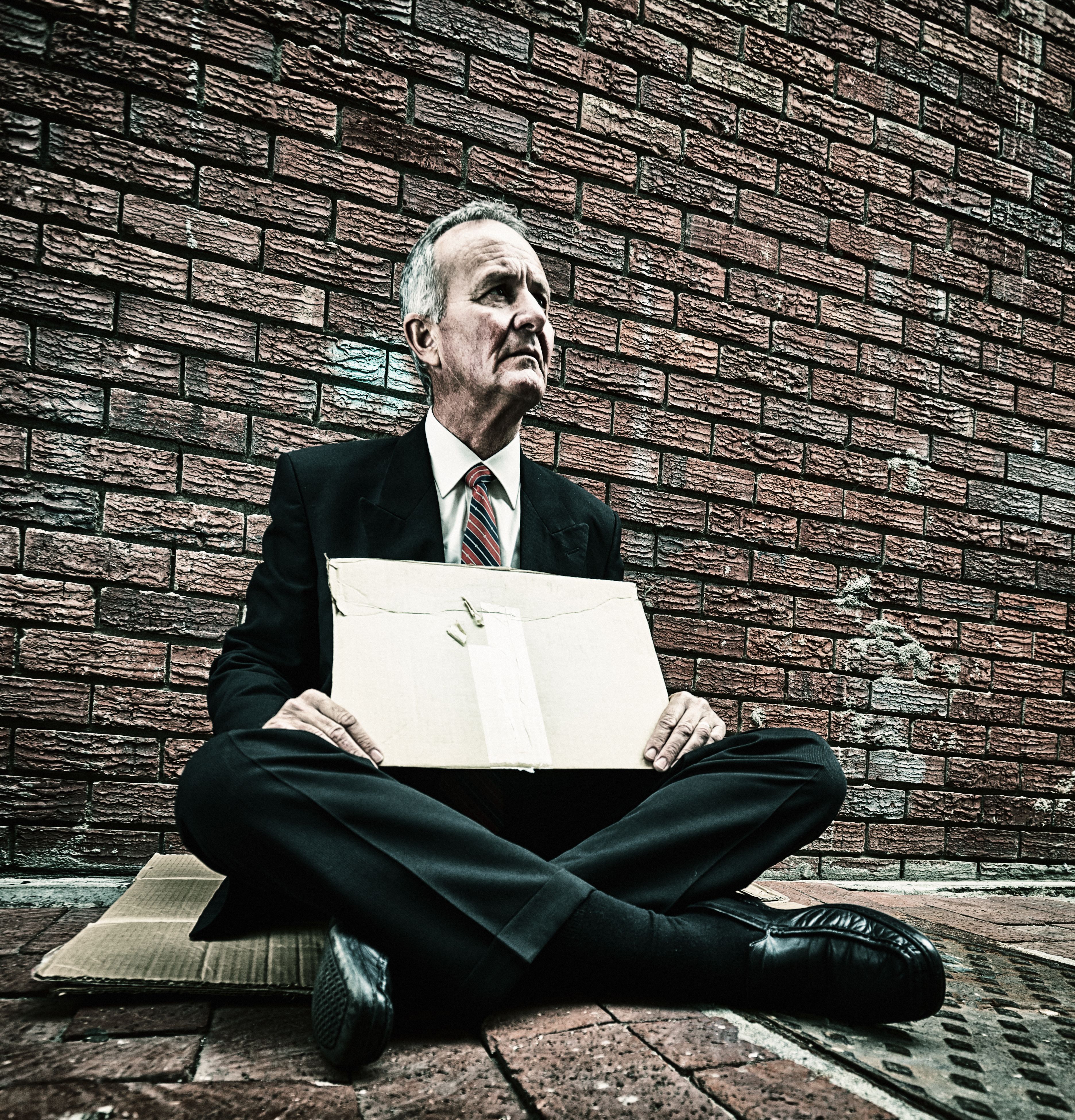 Businessman in a suit, fallen on hard times, begs in the street, holding a blank cardboard sign