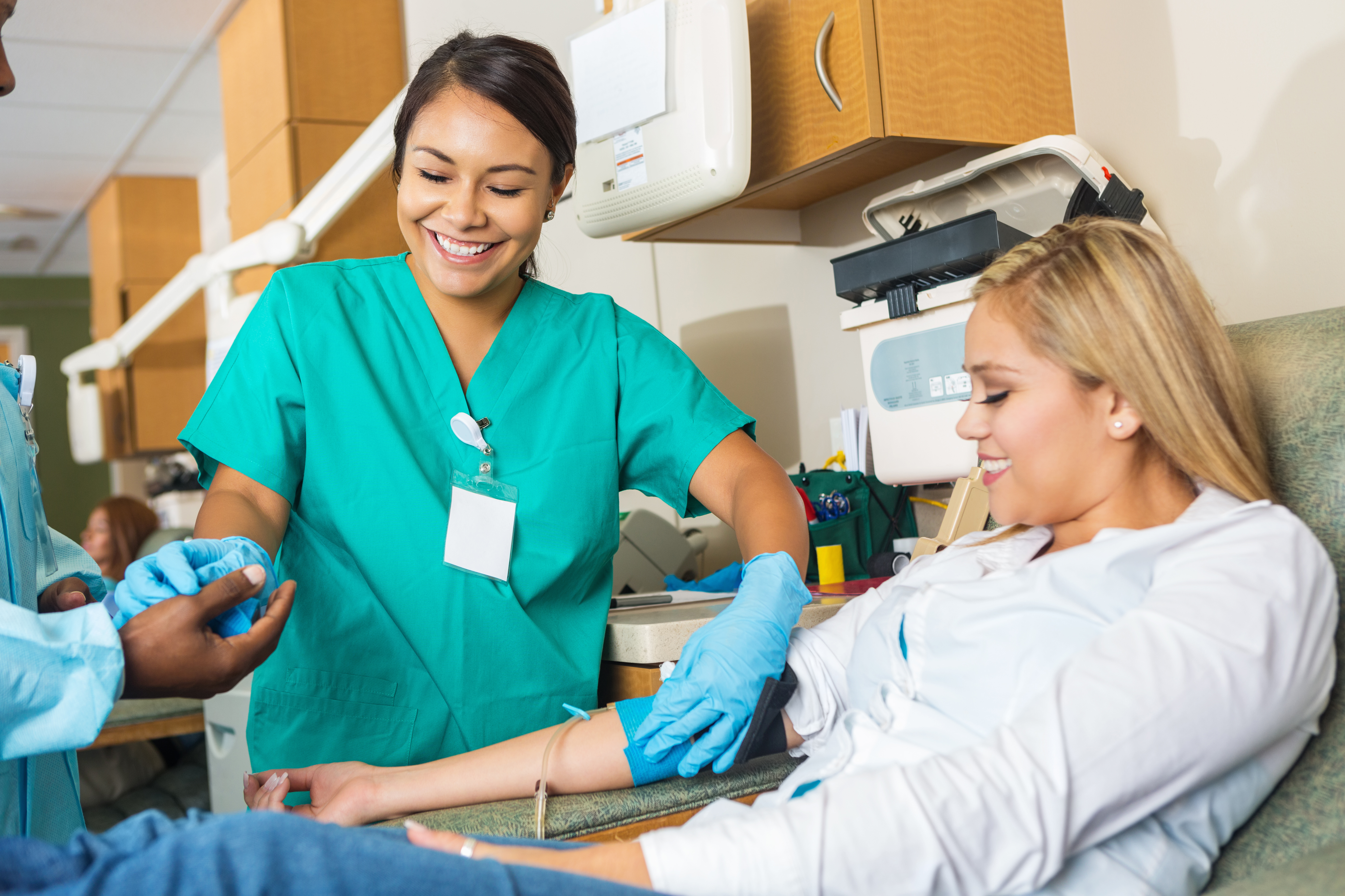 Nurse assisting coworker as she helps patient donating blood Nurse assisting coworker as she helps patient donating blood