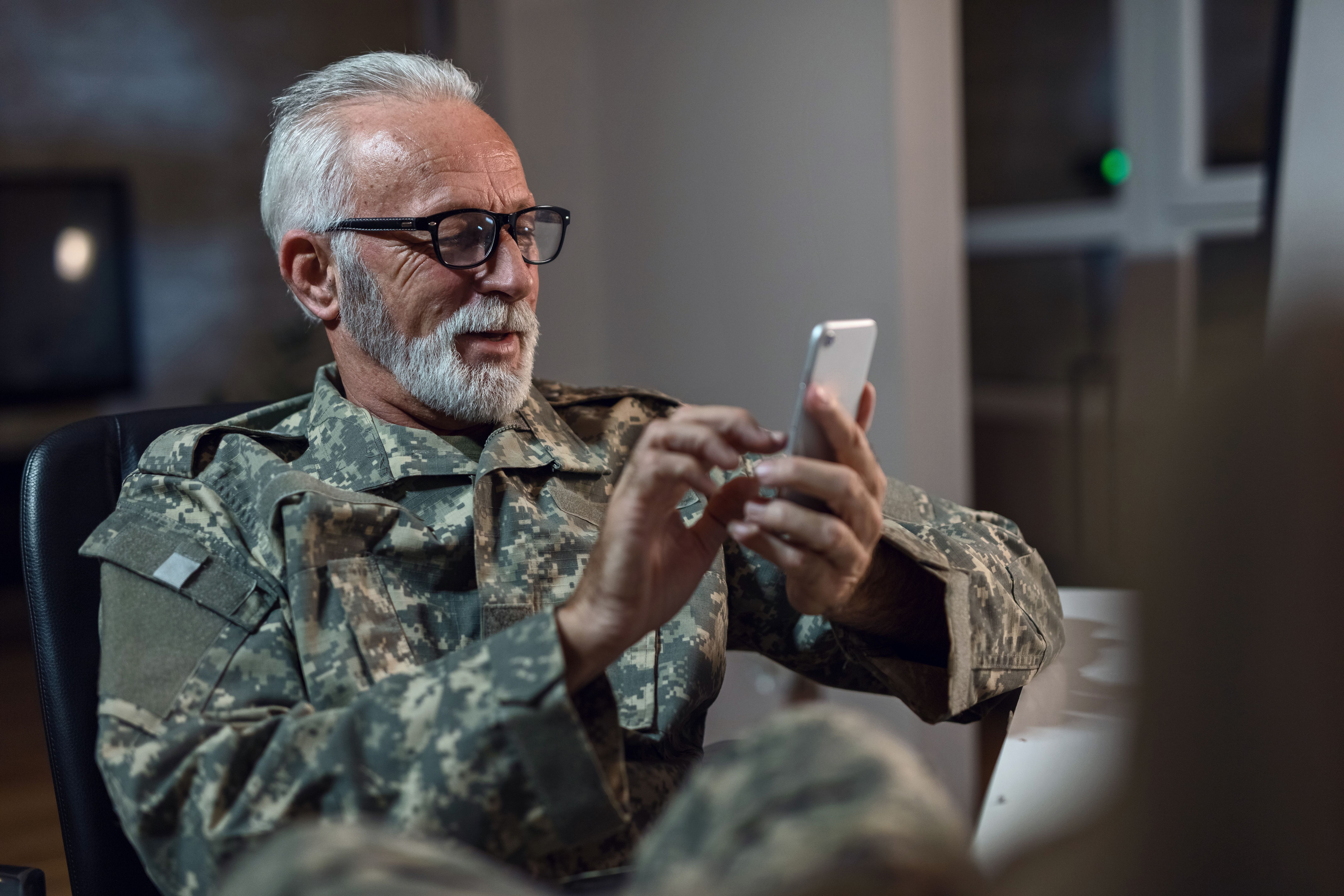 Smiling senior army soldier text messaging on smart phone.