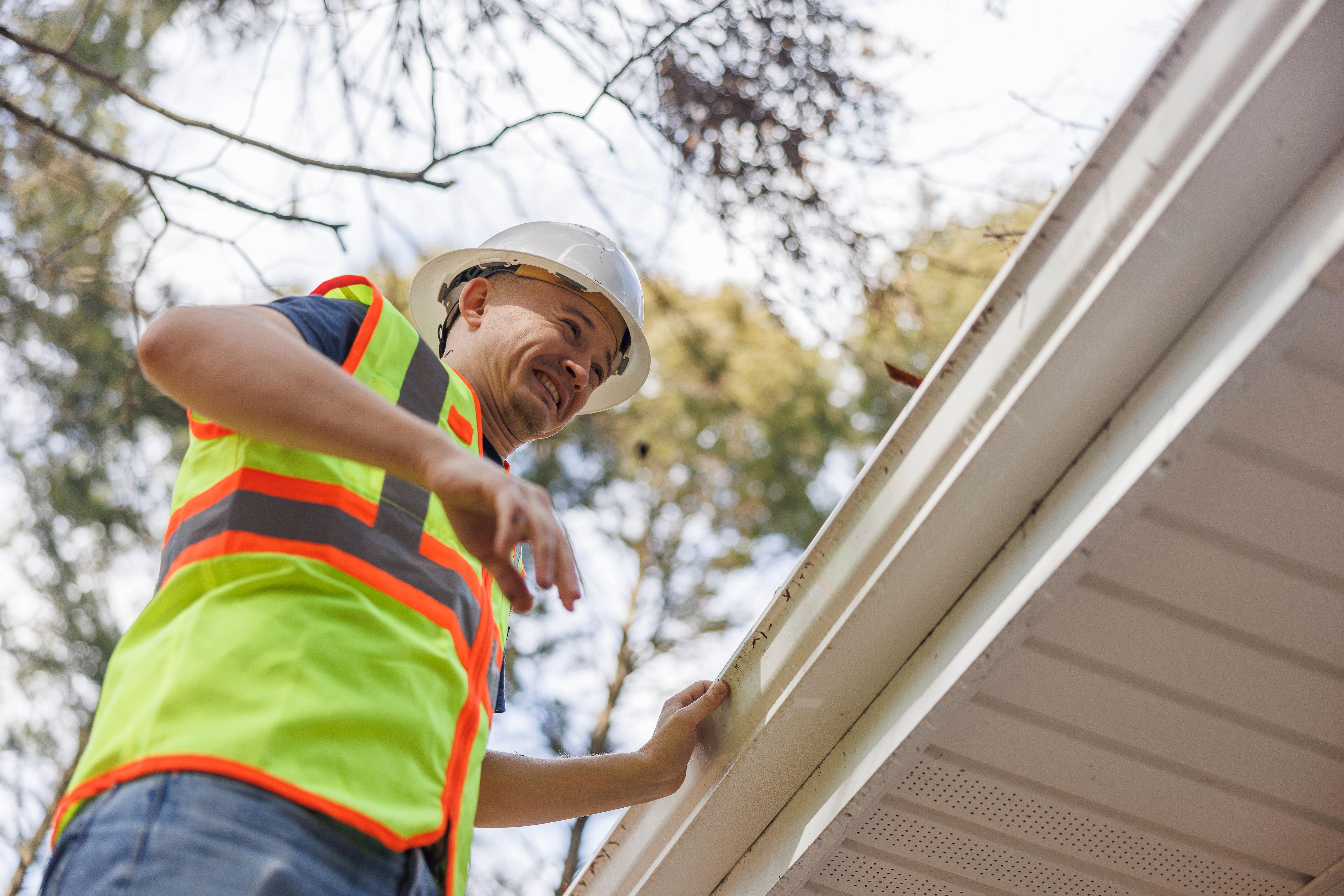 Worker disgustedly looks at the dirty roof gutter he must clean. Focus on the foreground with defocused background.