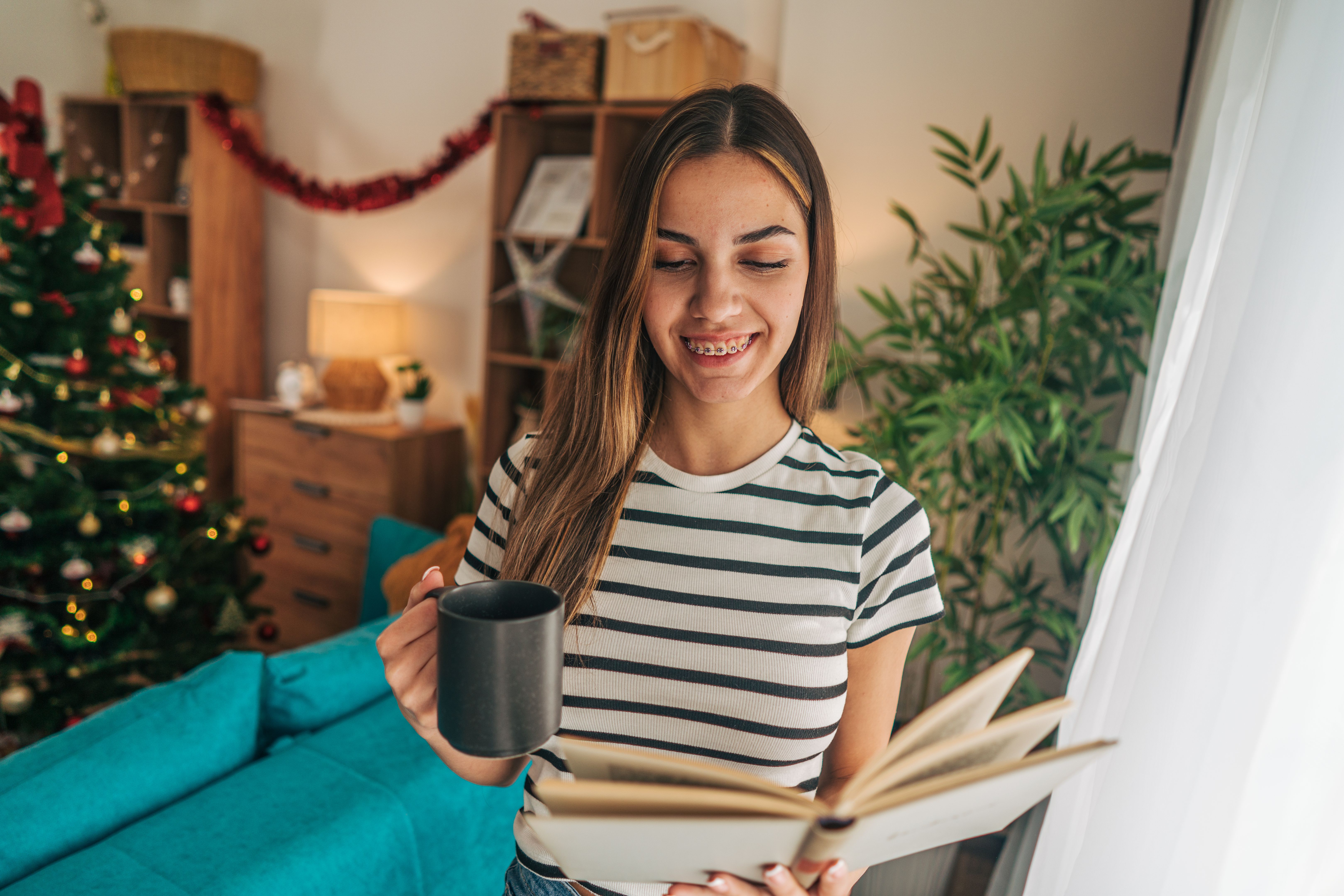 An 18-year-old girl standing by the window in the living room, enjoying the Christmas excitement. An 18-year-old girl standing by the window in the living room, enjoying the Christmas excitement.