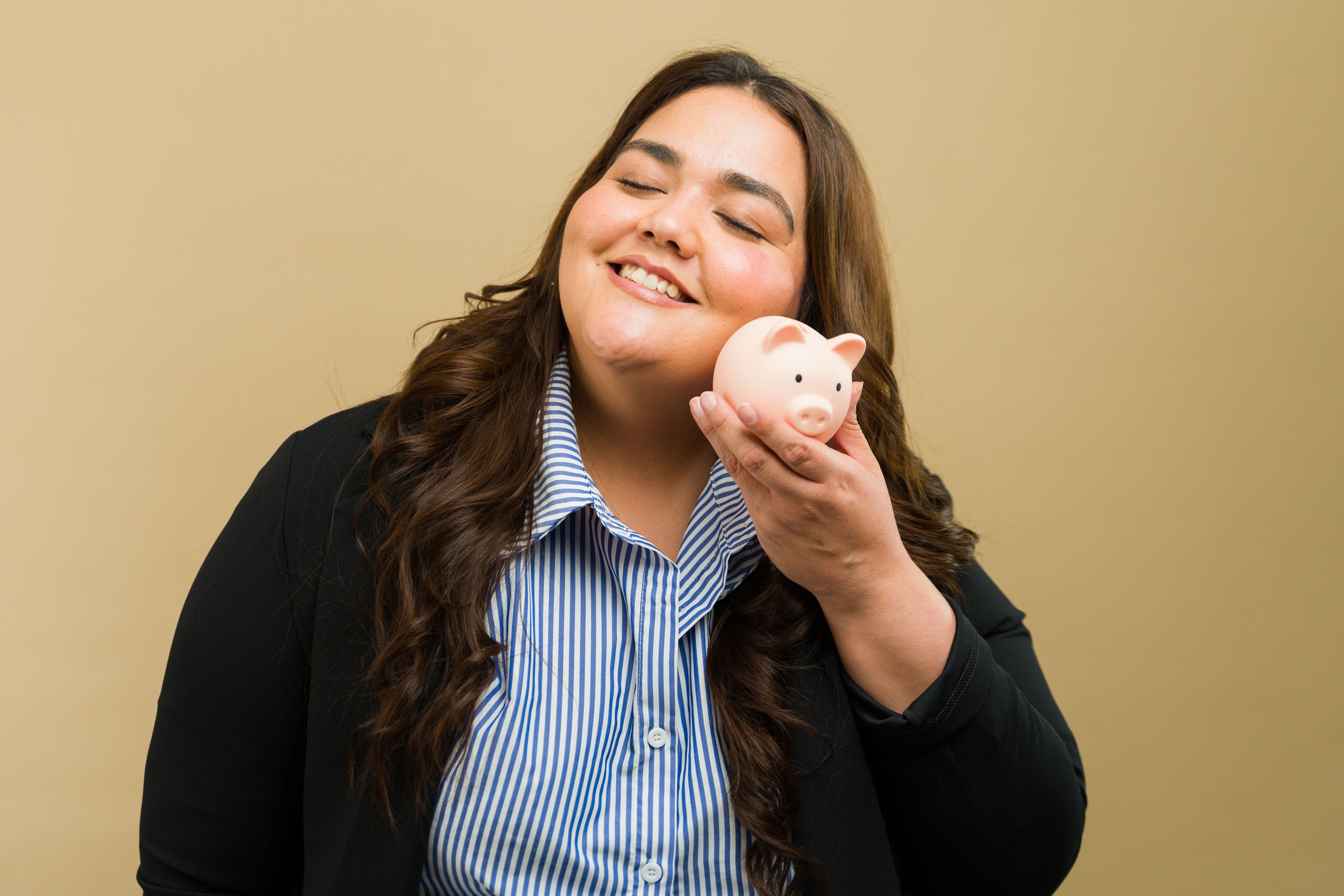 Happy plus-size woman poses with a piggy bank in a studio, representing financial stability and savings Happy plus-size woman poses with a piggy bank in a studio, representing financial stability and savings