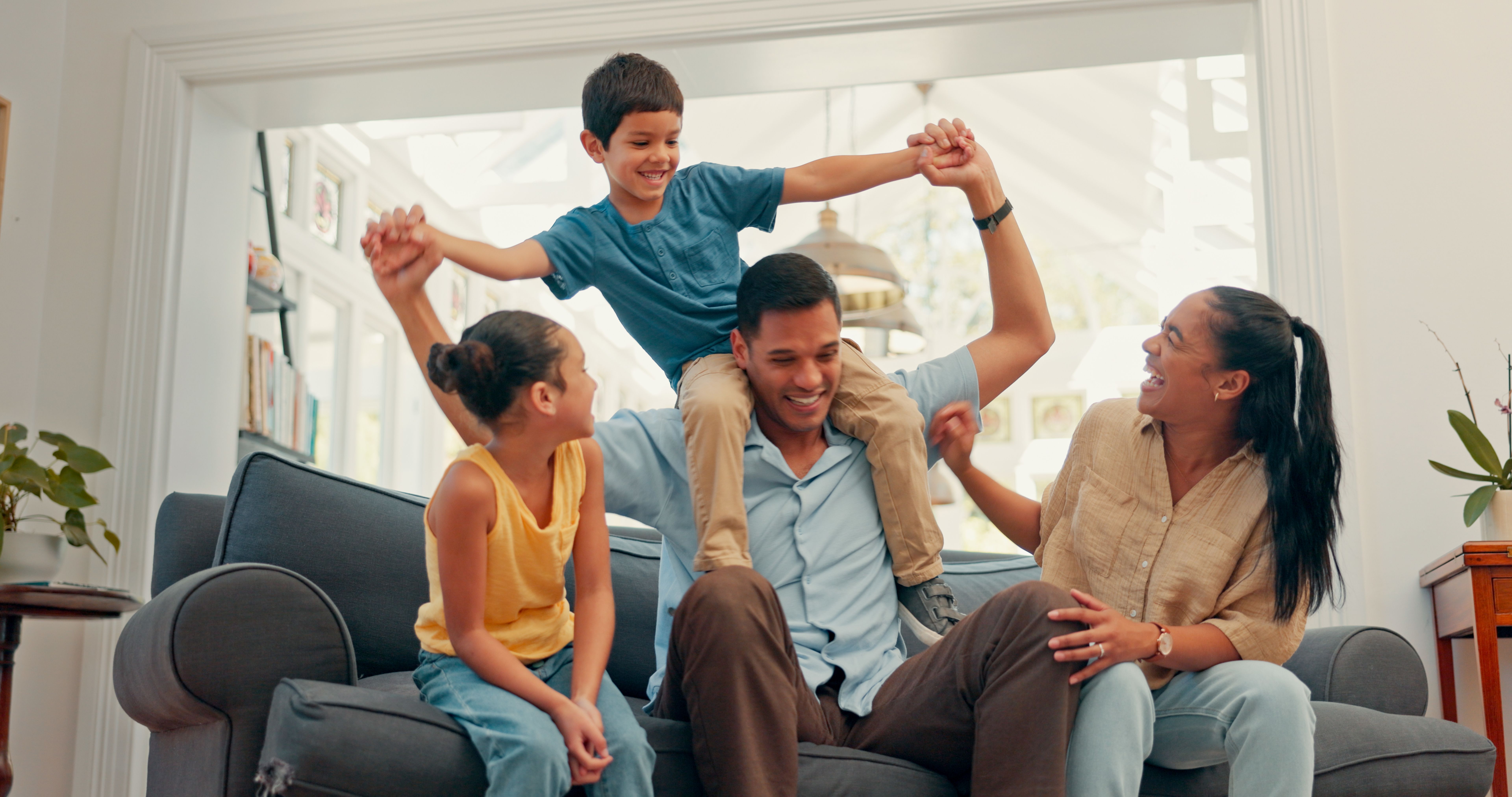 Happy family, love and airplane fun on a sofa with care, security and support while bonding at home. Flying, balance and excited kids with parents in a living room for playing shoulder games together
