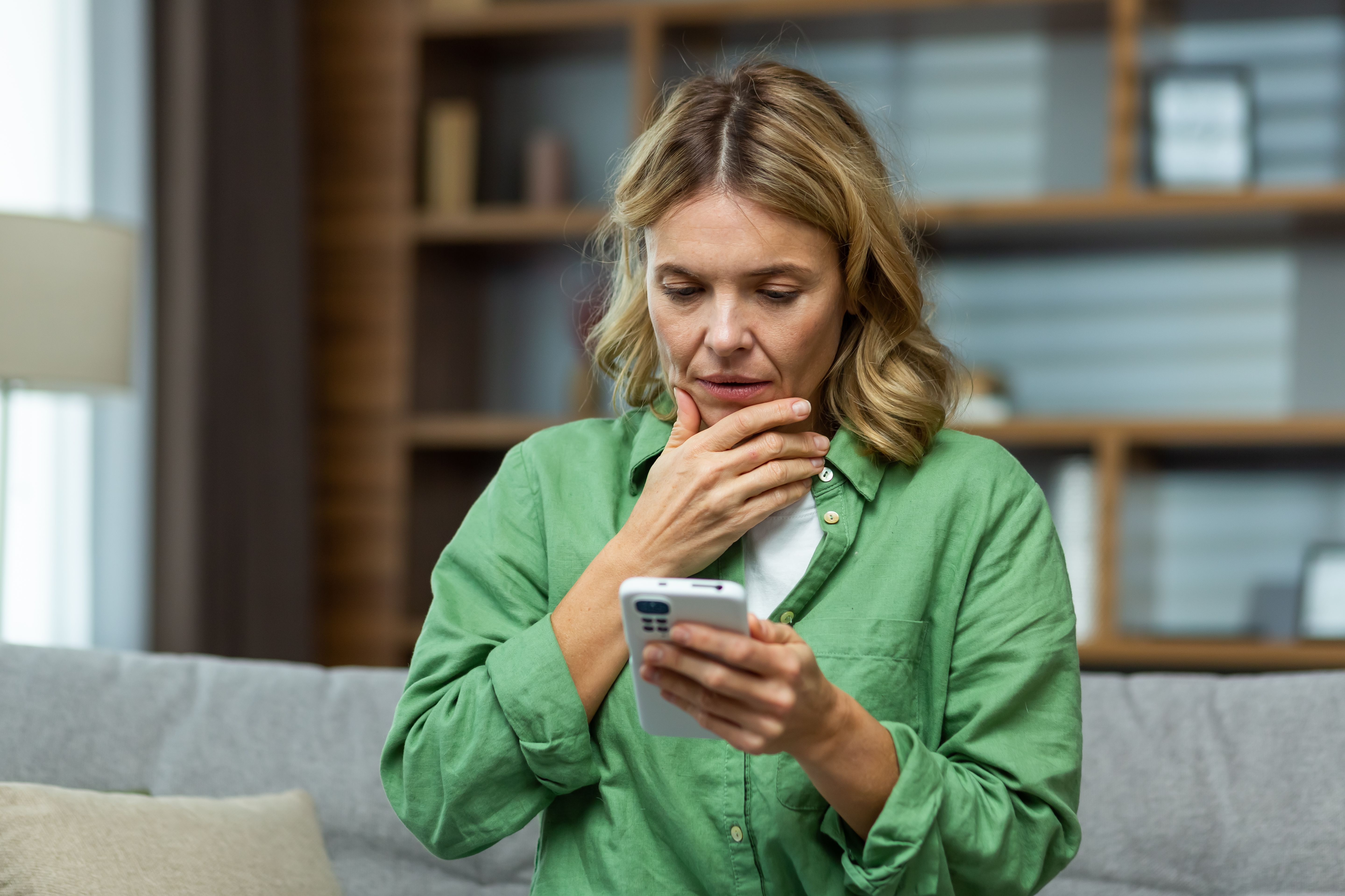 Close-up photo. Worried senior woman mother sitting on sofa at home and holding phone. Worries about children, writes and sends messages, calls, searches, waits at home