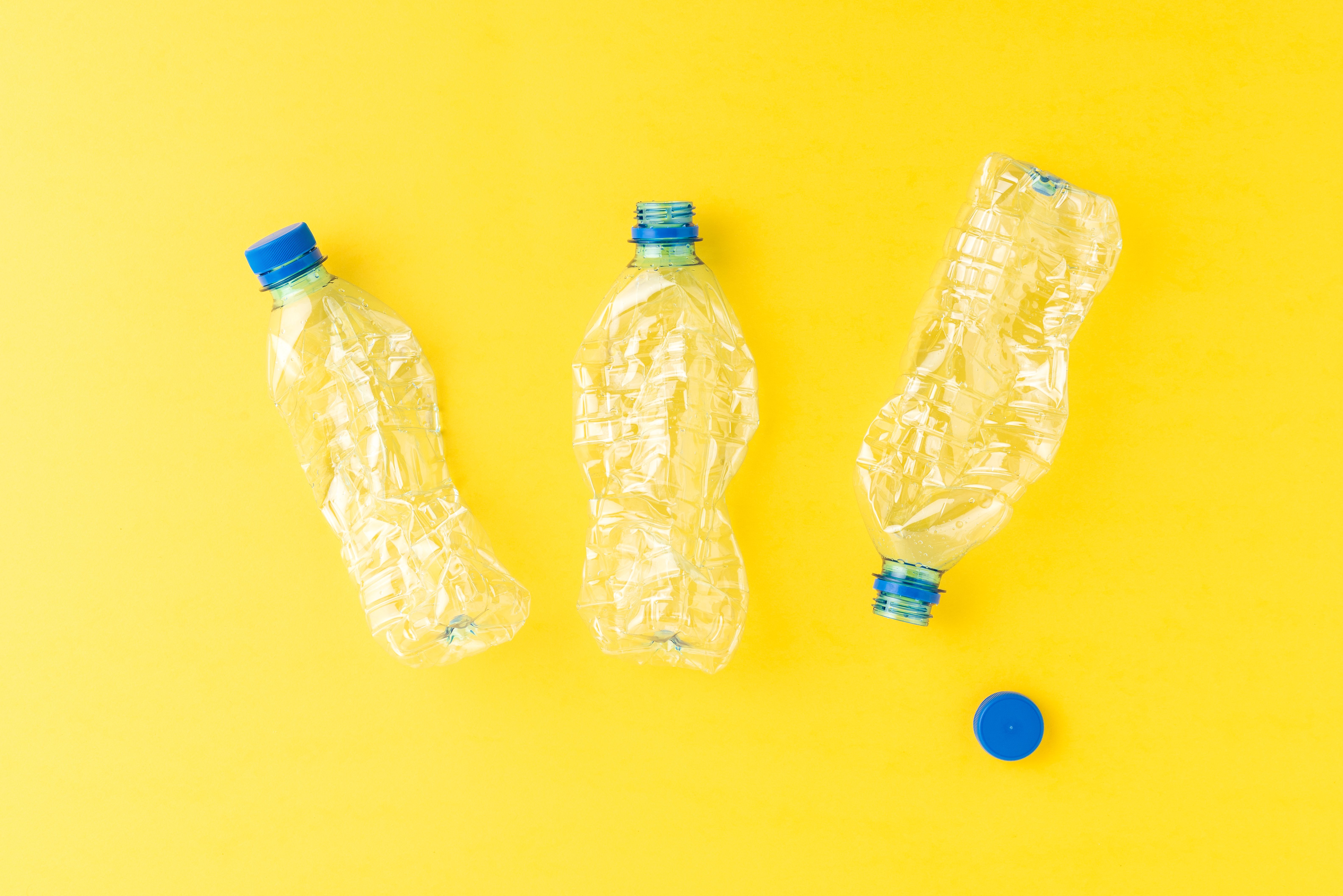 Used plastic bottles of water with caps on yellow background. Recycling concept. Flat lay