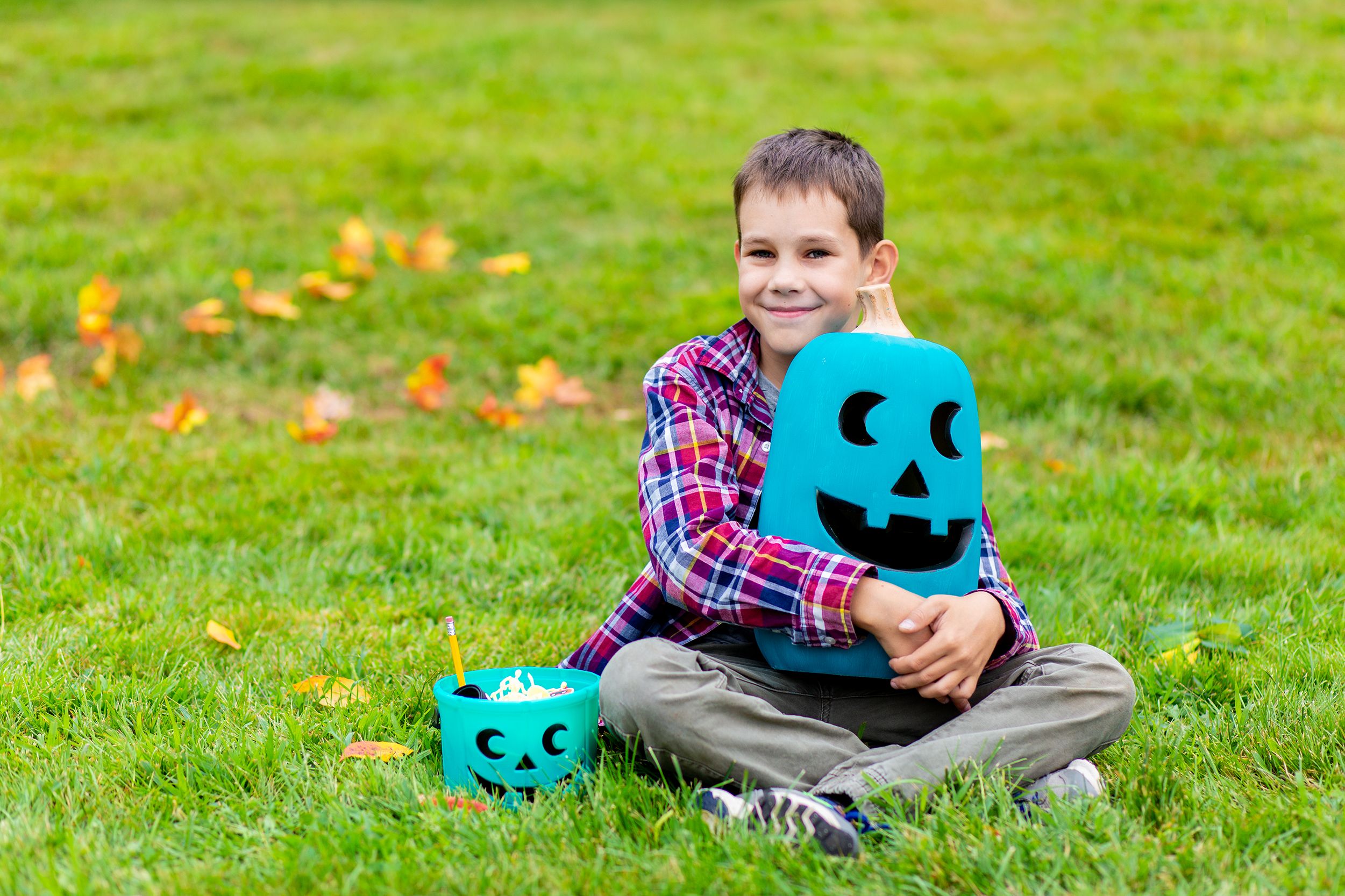 smiling boy hugs the teal pumpkin outside. teal bucket with non-food treats