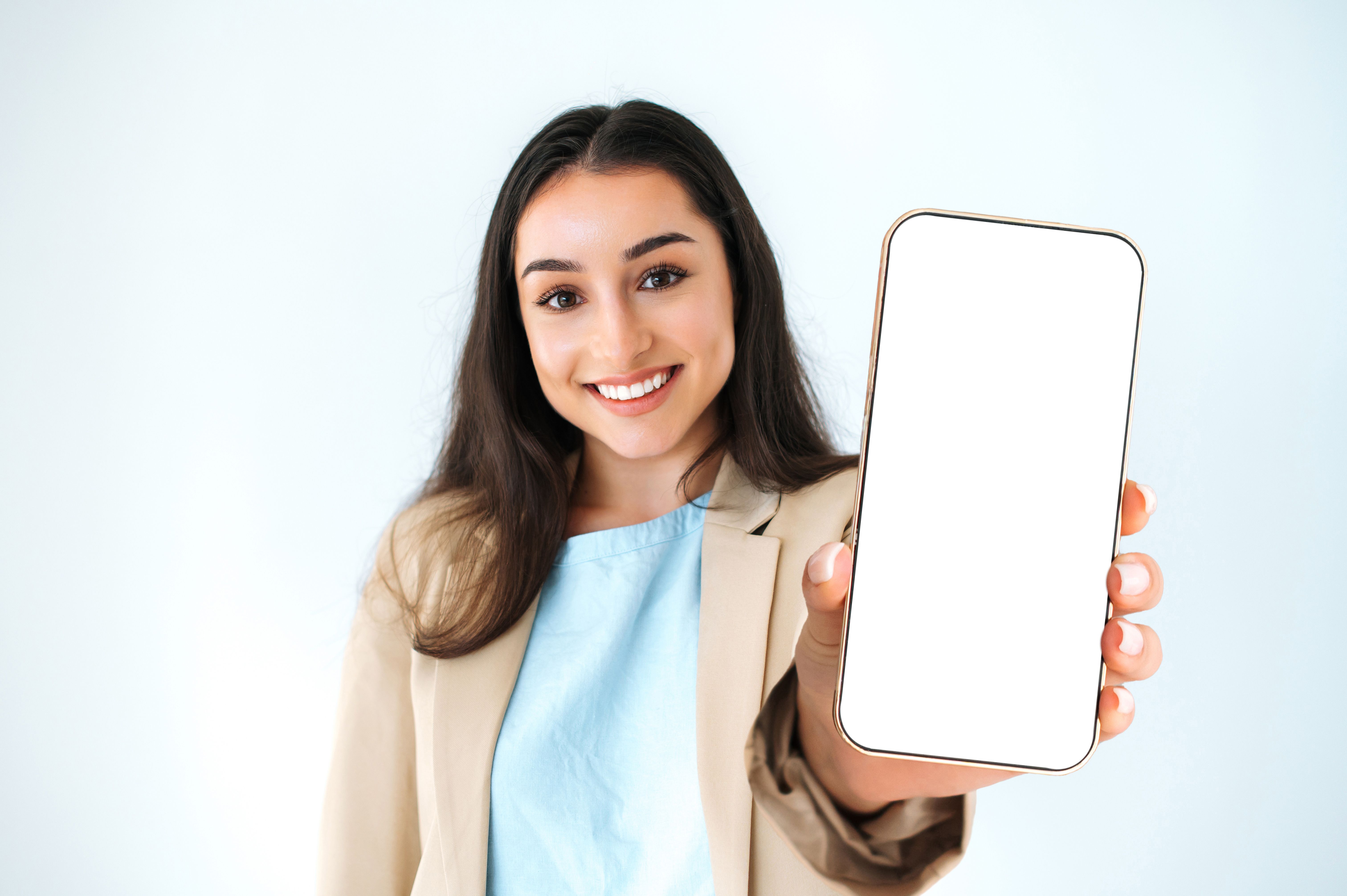 Copy-space concept. Happy indian or arabian woman in elegant suit, showing smart phone with empty white mock-up screen for advertising, standing on isolated white background, looks at camera, smiling Copy-space concept. Happy indian or arabian woman in elegant suit, showing smart phone with empty white mock-up screen for advertising, standing on isolated white background, looks at camera, smiling