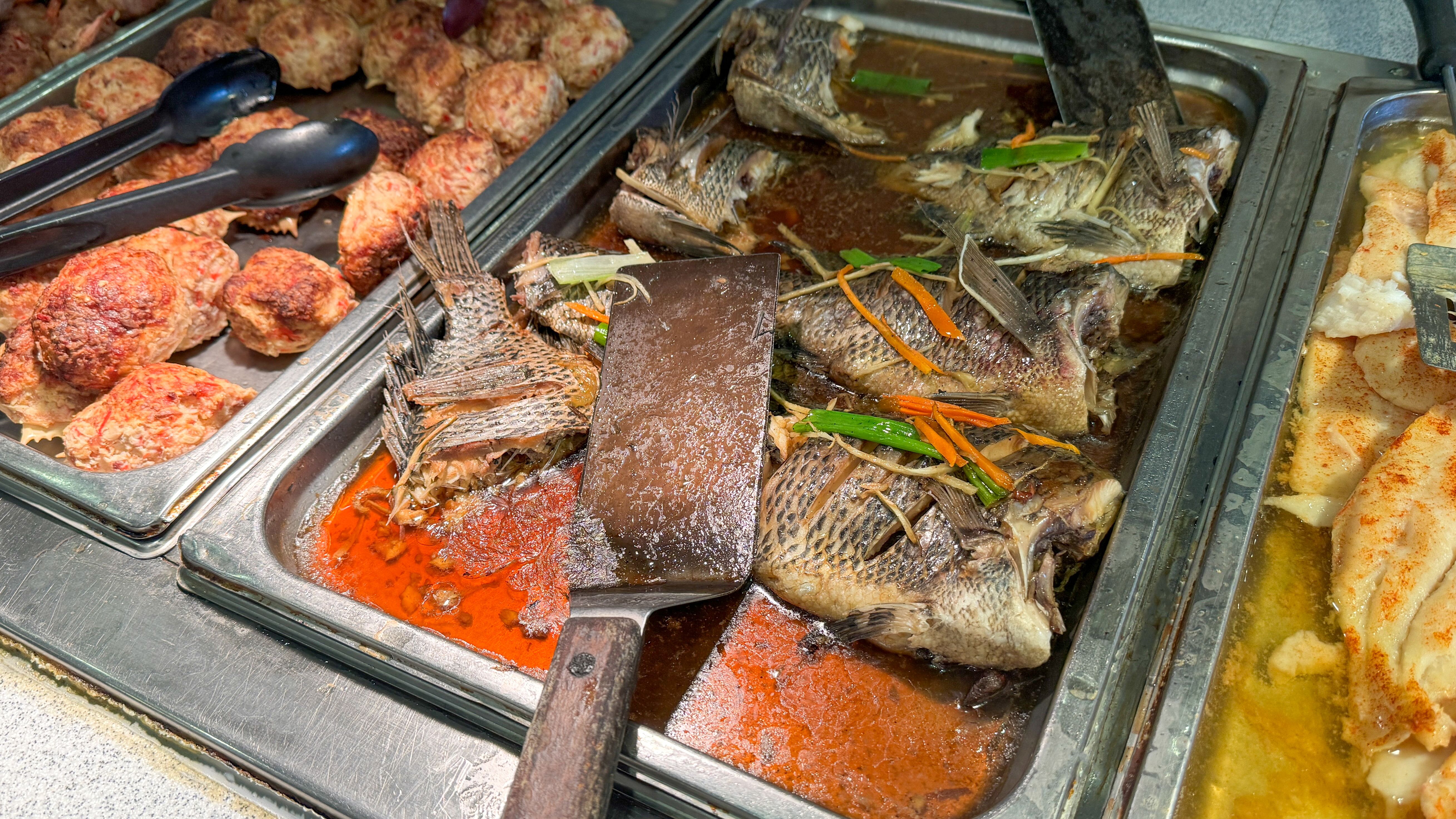 a buffet display featuring cooked whole fish in a flavorful sauce, meatballs, and filleted fish, ready to be served a buffet display featuring cooked whole fish in a flavorful sauce, meatballs, and filleted fish, ready to be served