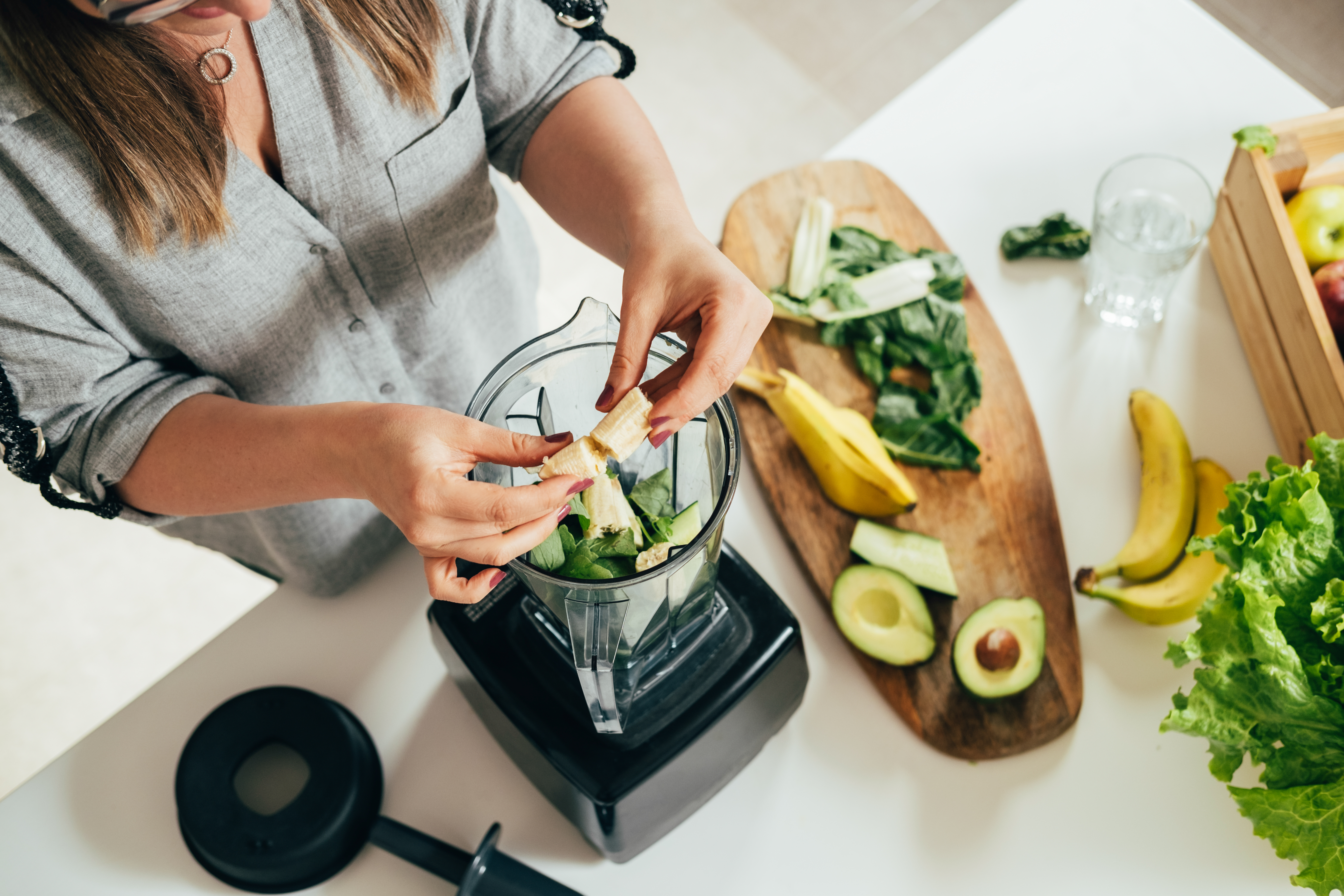 Woman is preparing a healthy detox drink in a blender - a green smoothie with fresh fruits, green spinach and avocado Woman is preparing a healthy detox drink in a blender - a green smoothie with fresh fruits, green spinach and avocado