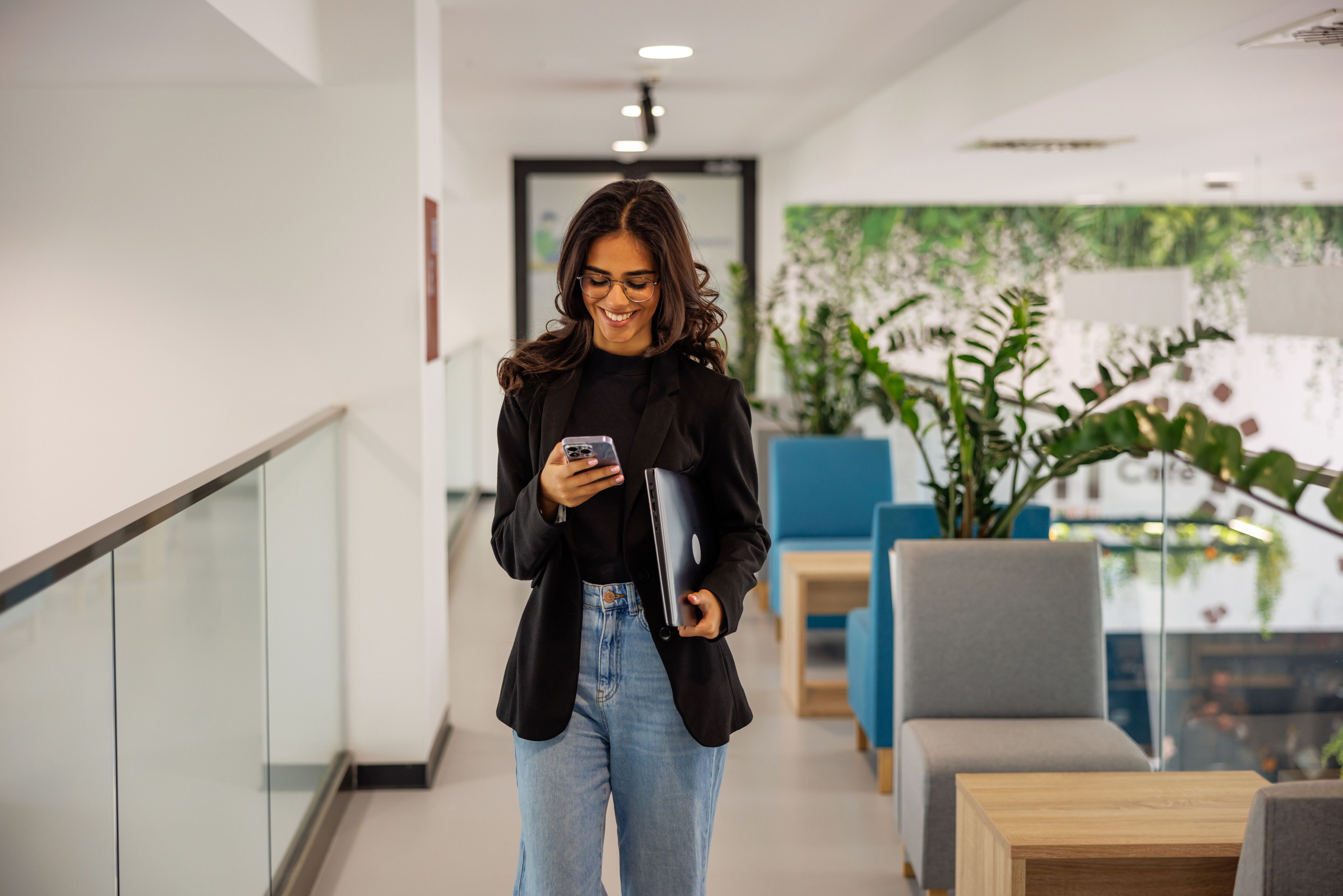 Successful young woman using smartphone while walking in business building