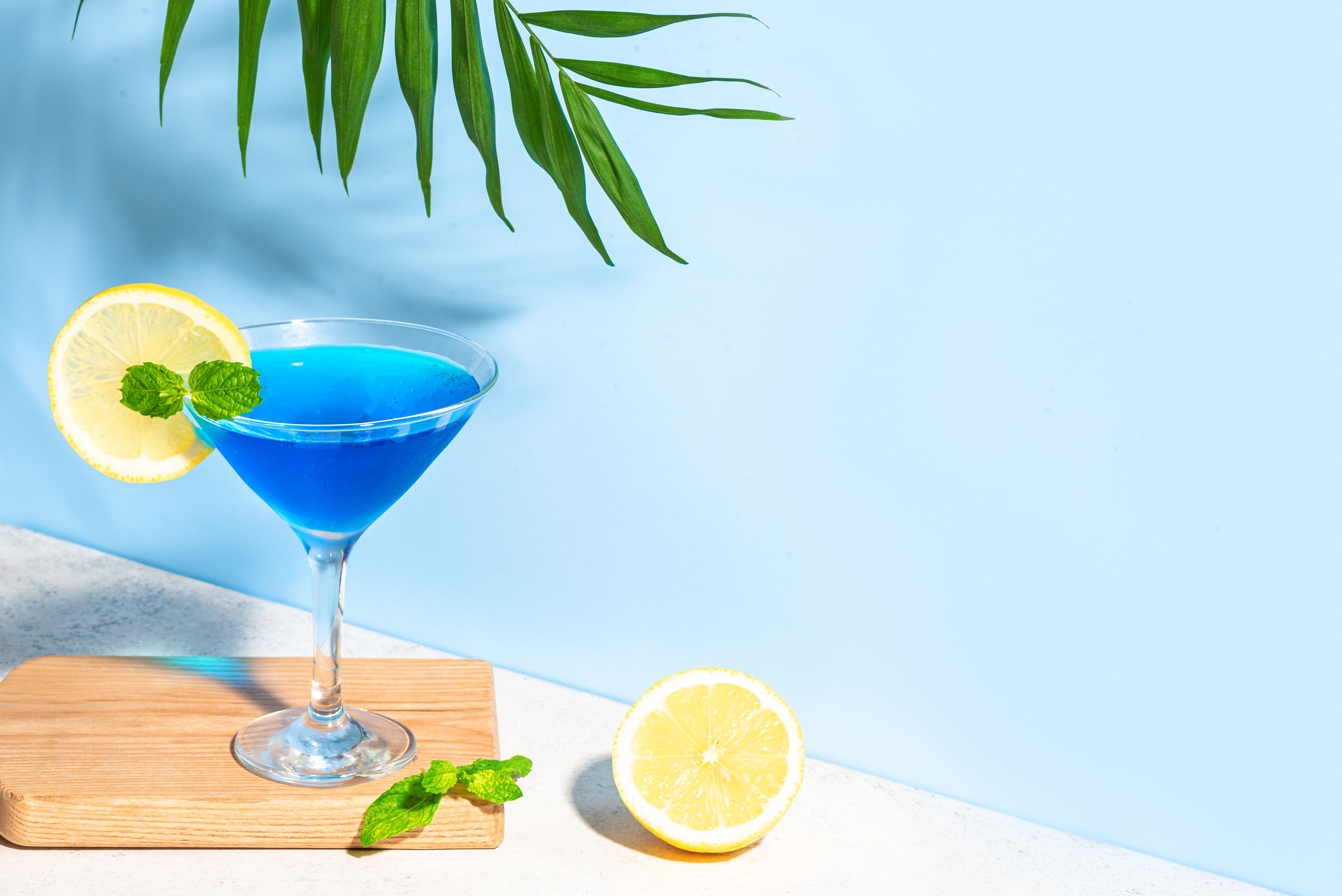 Blue summer cocktail with lemon and palm leaf