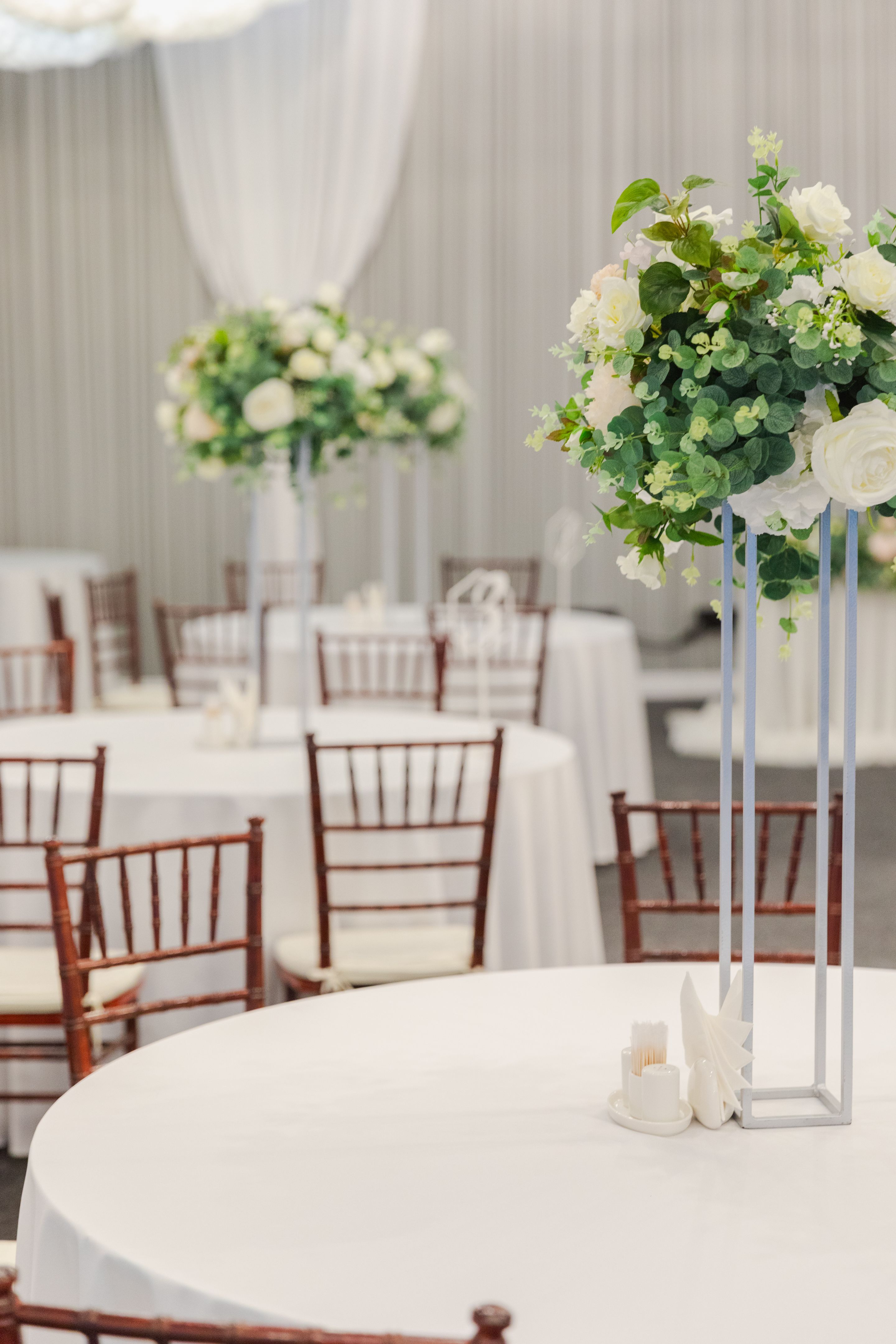 Decorated interior for festive event. Fancy table set for dinner with white flower composition in restaurant, luxury interior background. Wedding elegant banquet decoration arranged by catering service.