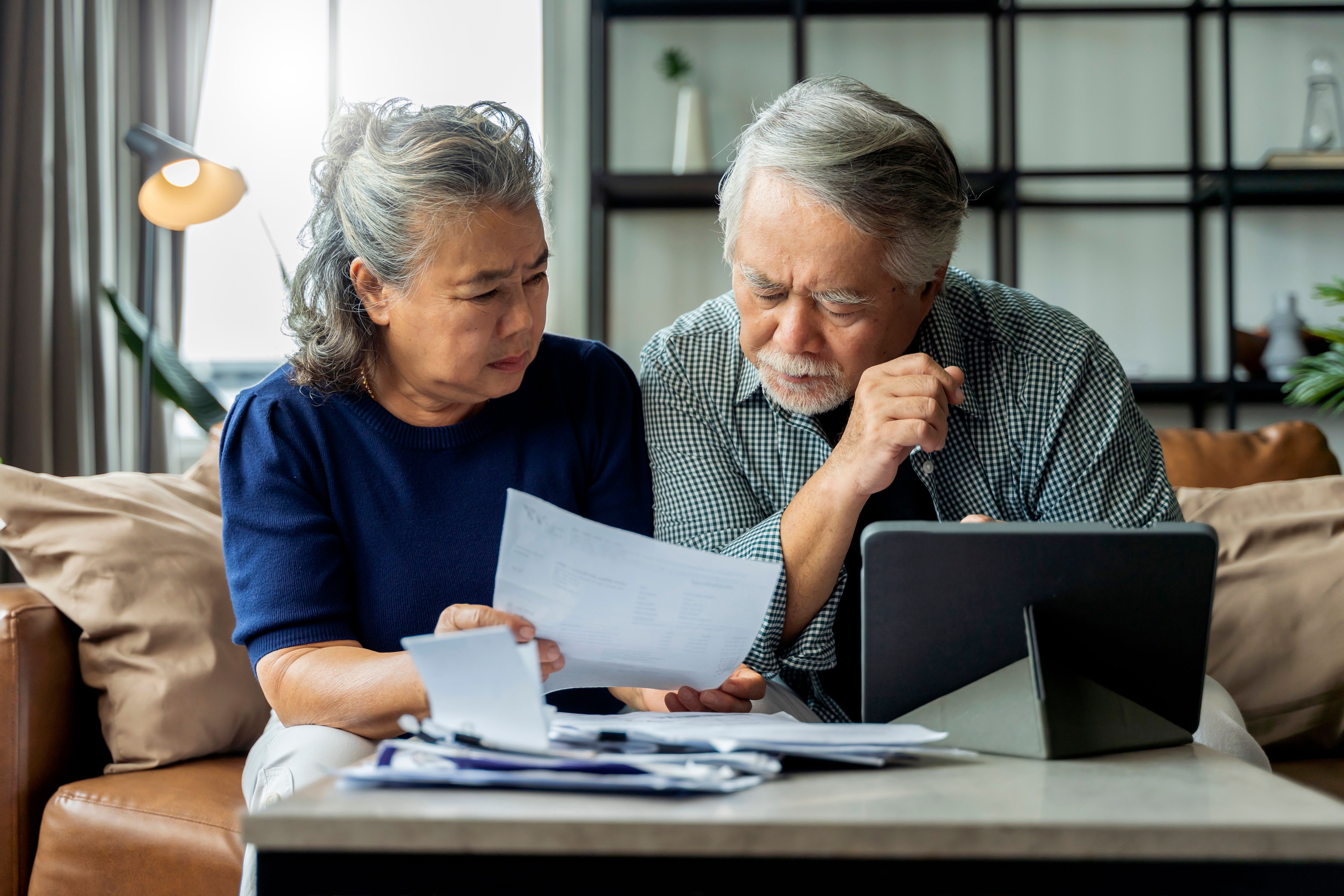 old retired asian senior couple checking and calculate financial billing together on sofa involved in financial paperwork, paying taxes online using e-banking laptop at living room home background old retired asian senior couple checking and calculate financial billing together on sofa involved in financial paperwork, paying taxes online using e-banking laptop at living room home background