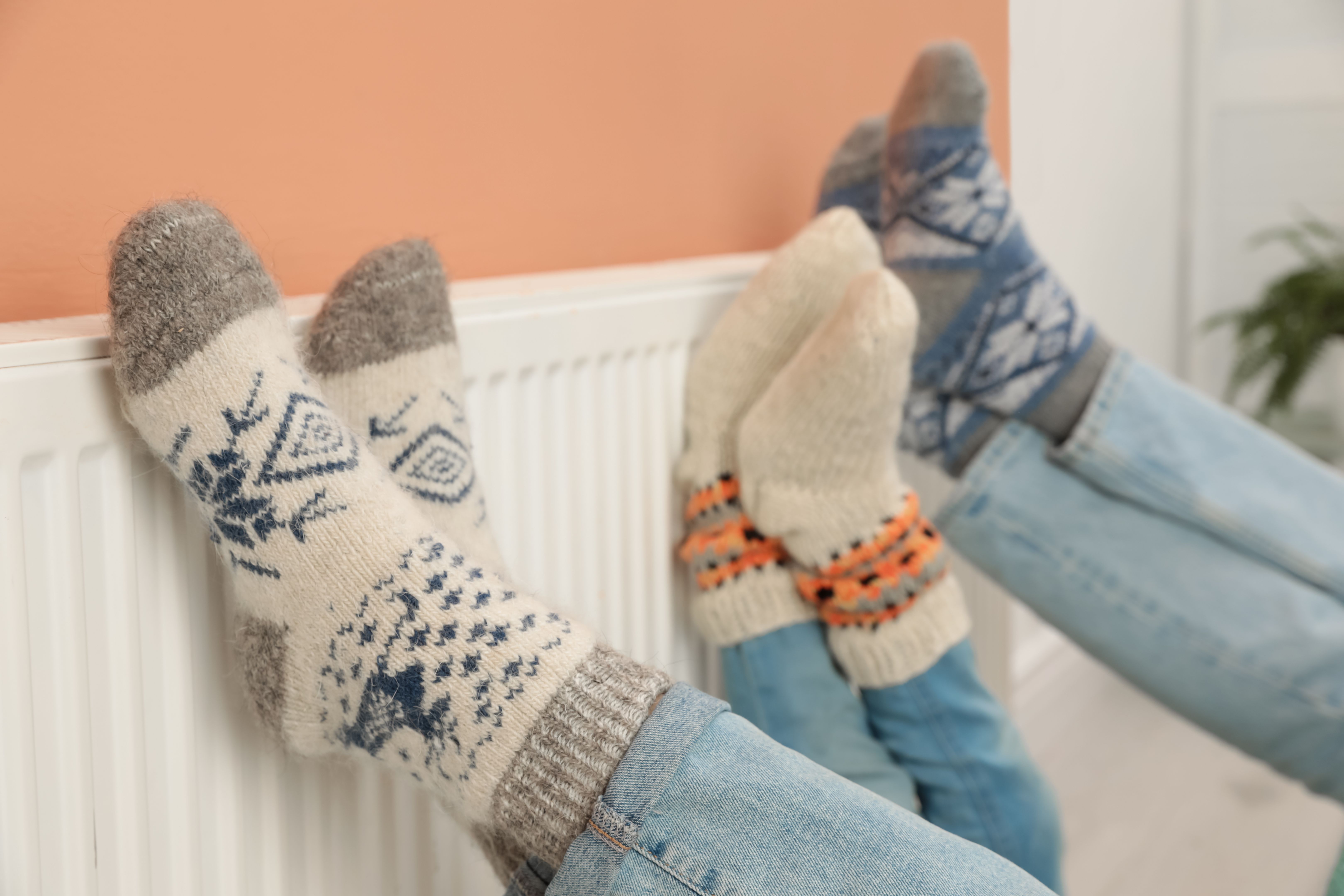 Family warming legs on heating radiator near color wall, closeup Family warming legs on heating radiator near color wall, closeup