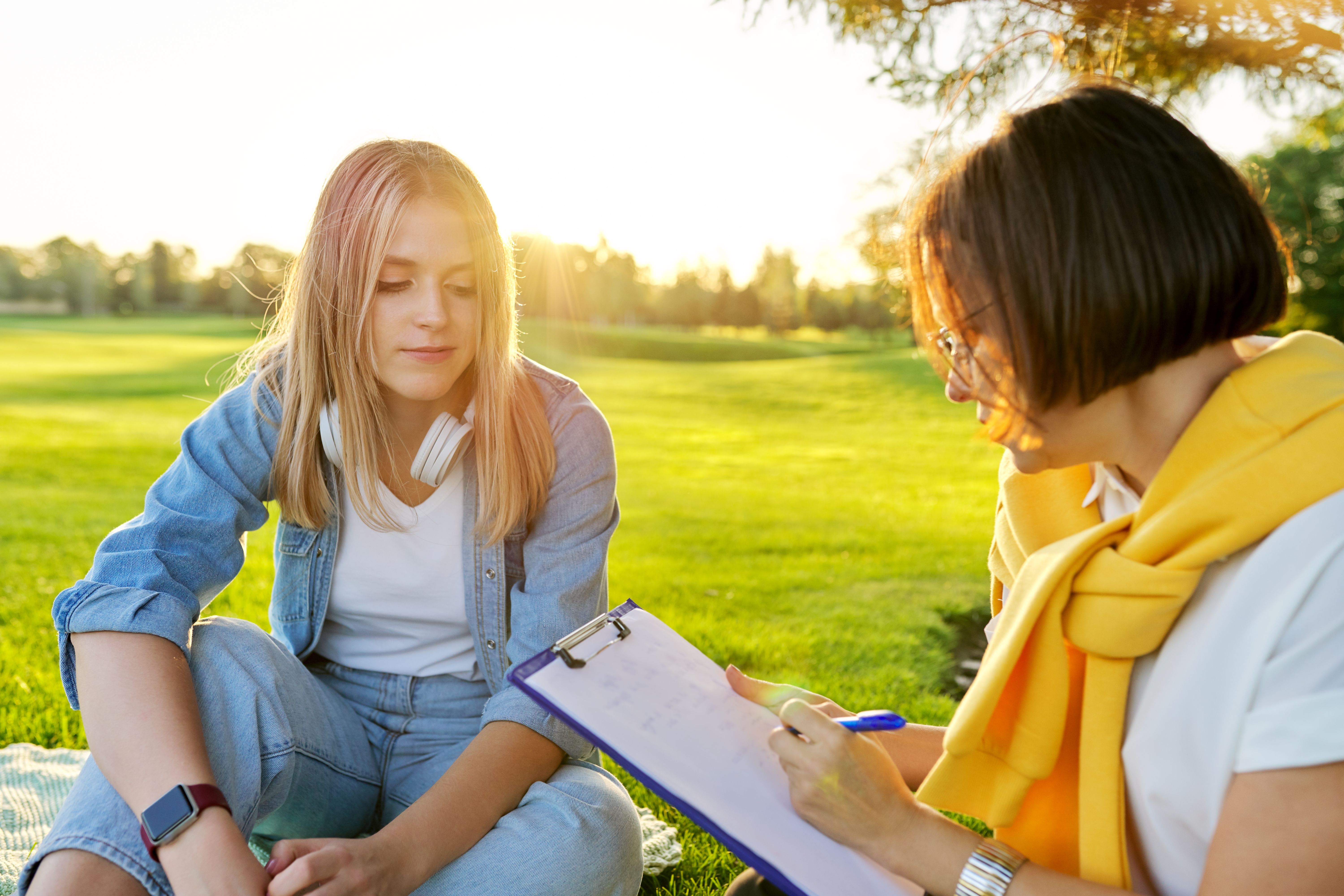 Conversation of young woman with psychologist, social worker, outdoor at meeting in park on lawn Conversation of young woman with psychologist, social worker, outdoor at meeting in park on lawn