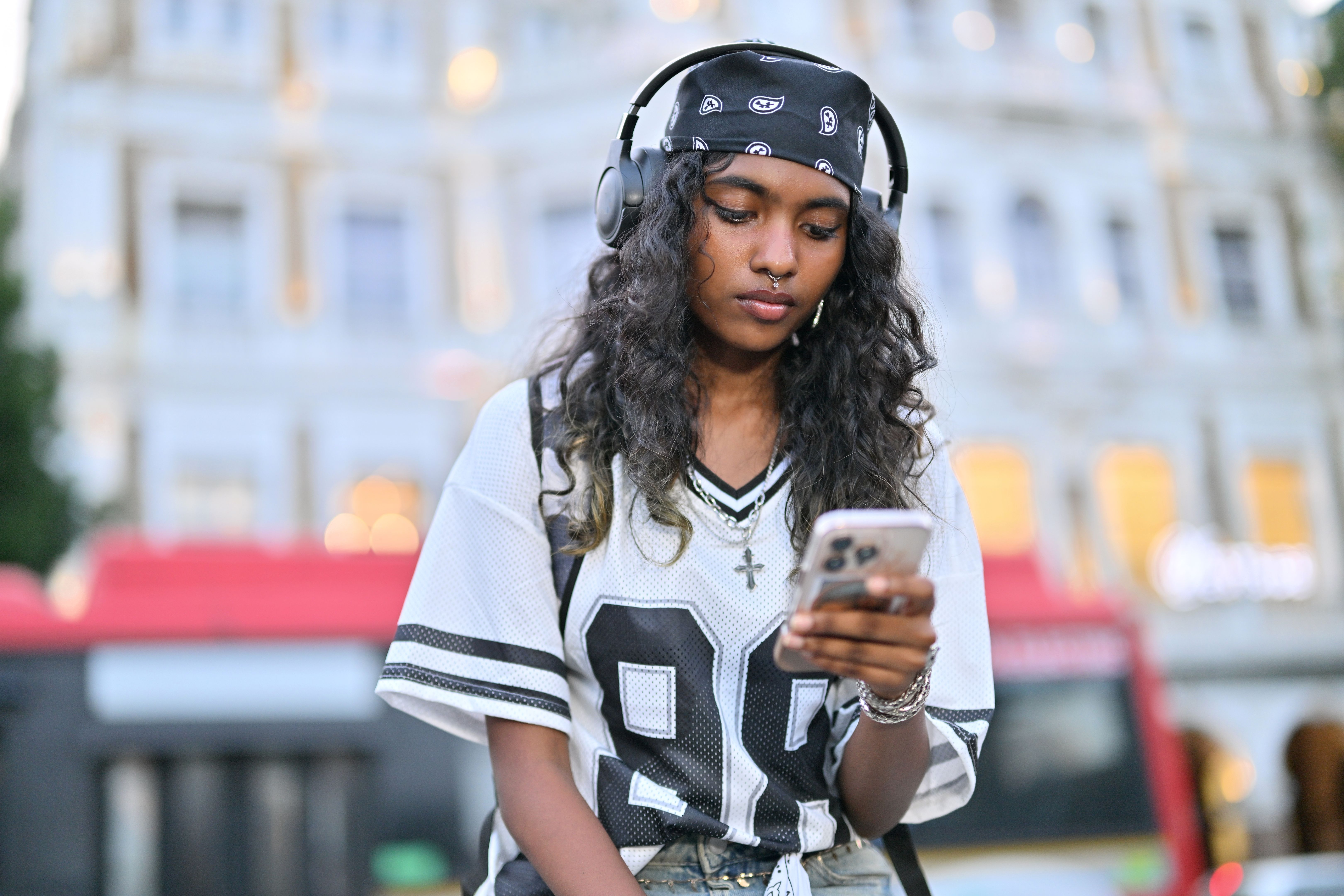 A teenage girl checks her phone while listening to music outdoors.