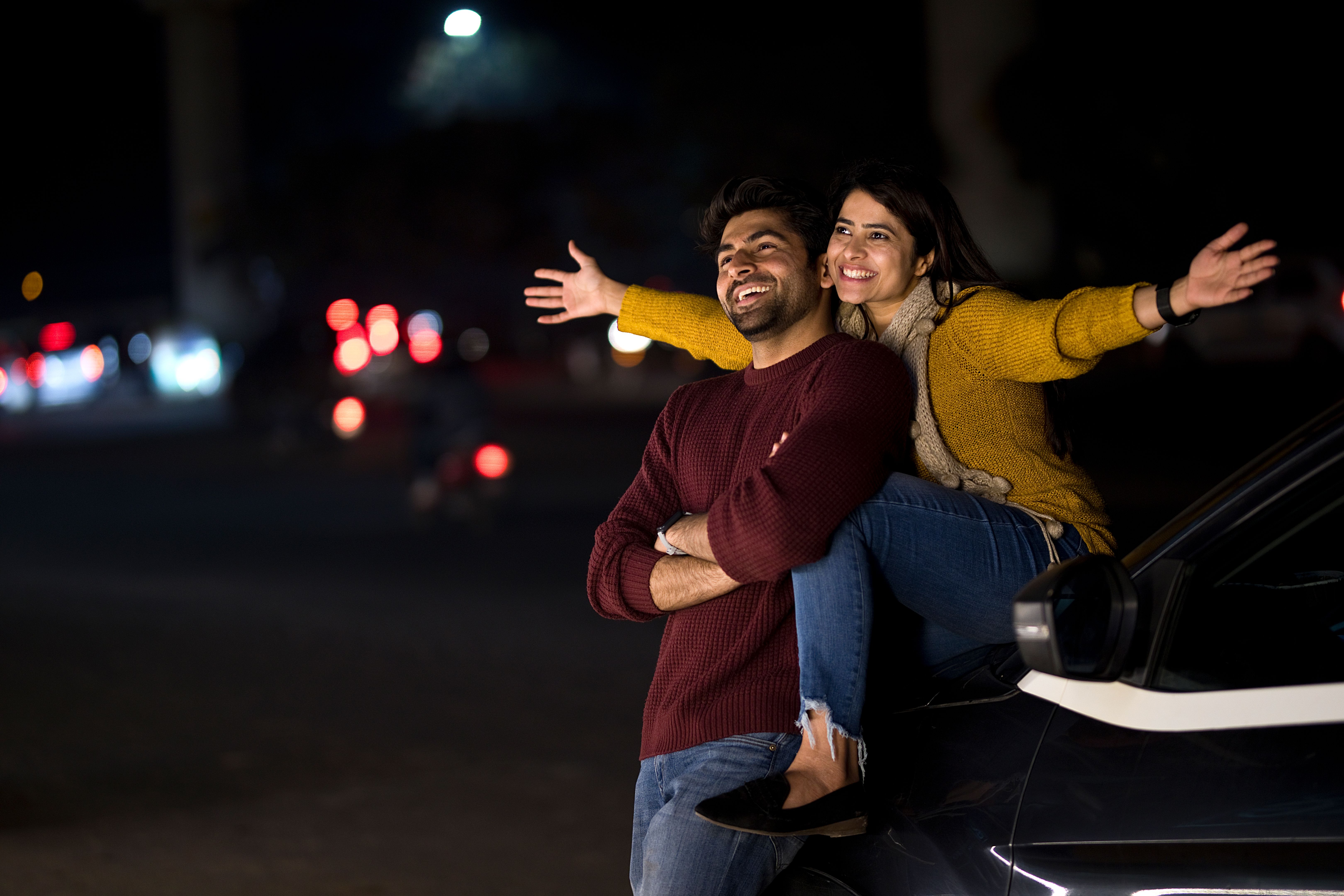 Carefree couple spending leisure time on car hood outdoors at night