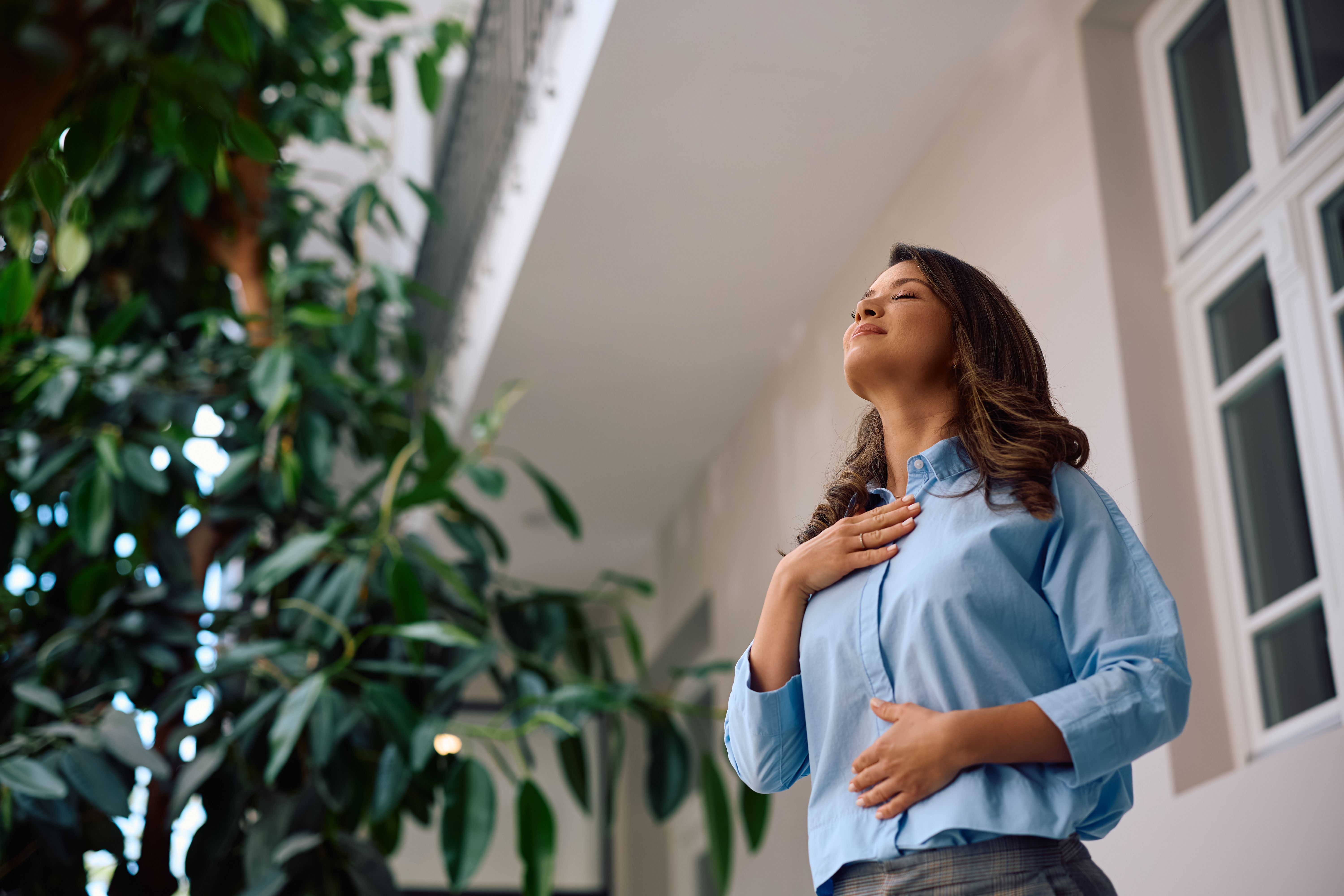 Relaxed businesswoman breathing with eyes closed in office building atrium. Relaxed businesswoman breathing with eyes closed in office building atrium.