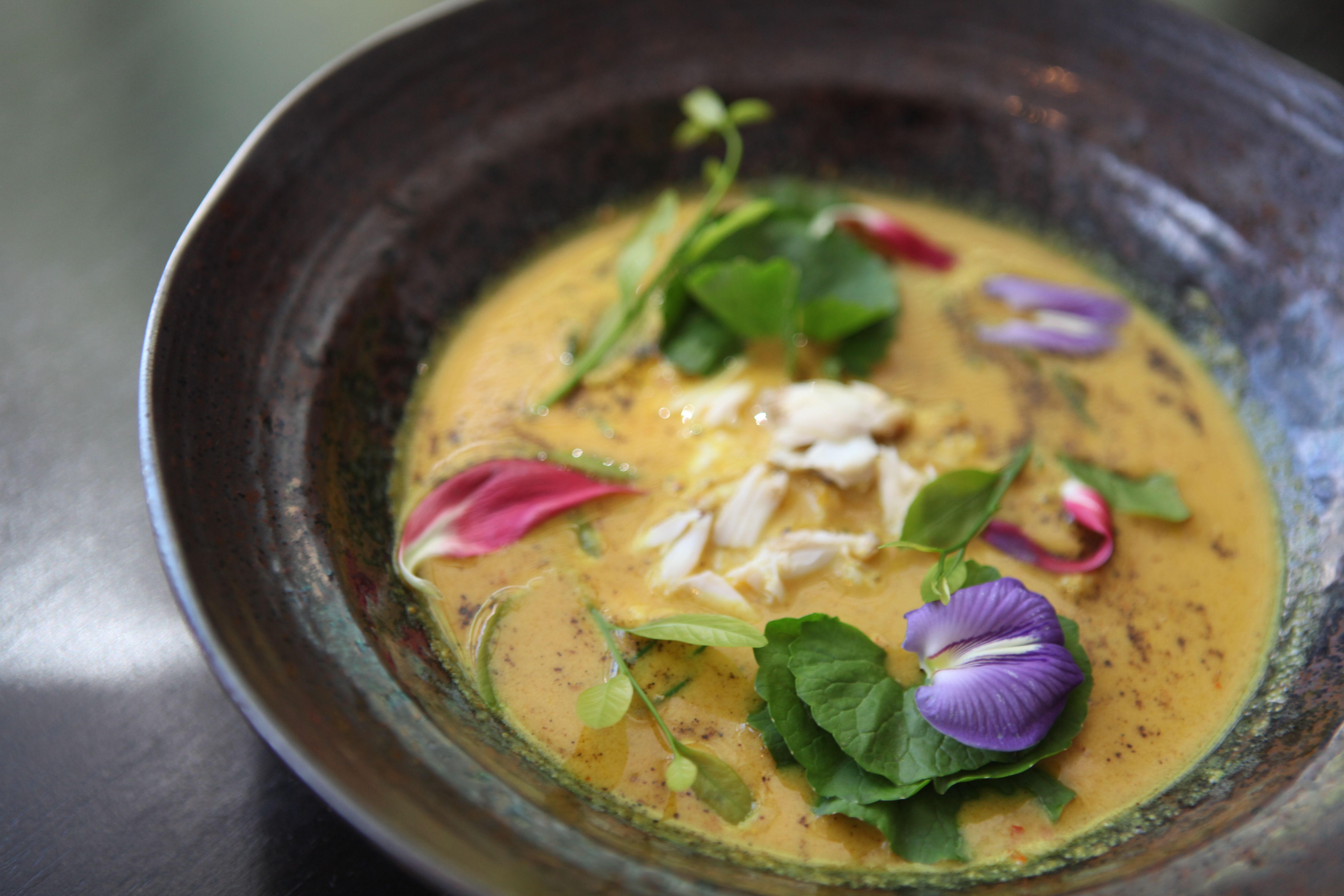 A beautiful and colorful bowl of Thai crab curry garnished with edible flowers at a Michelin Starred restaurant